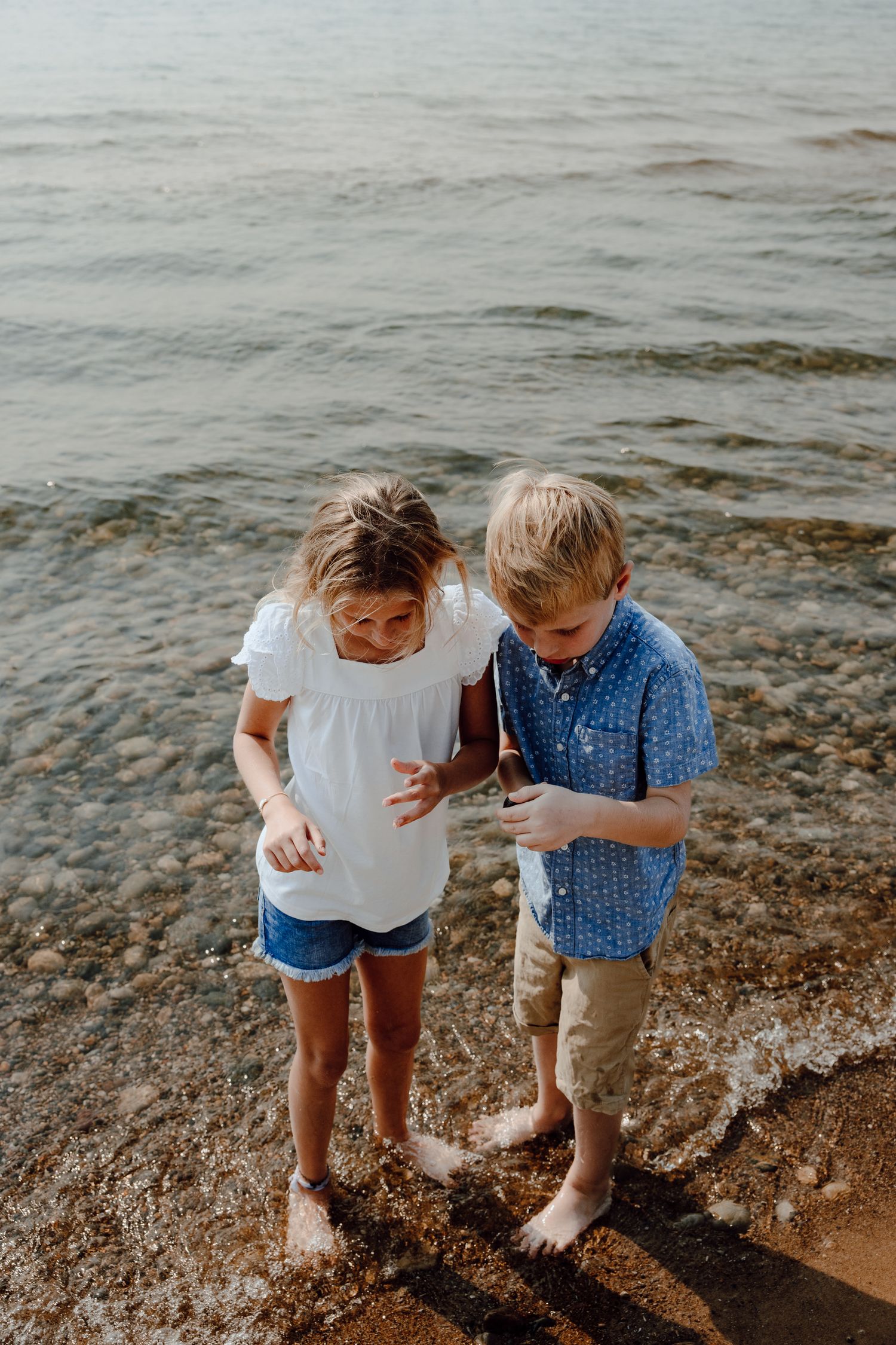 Two children explore and play in the sand at the water's edge.