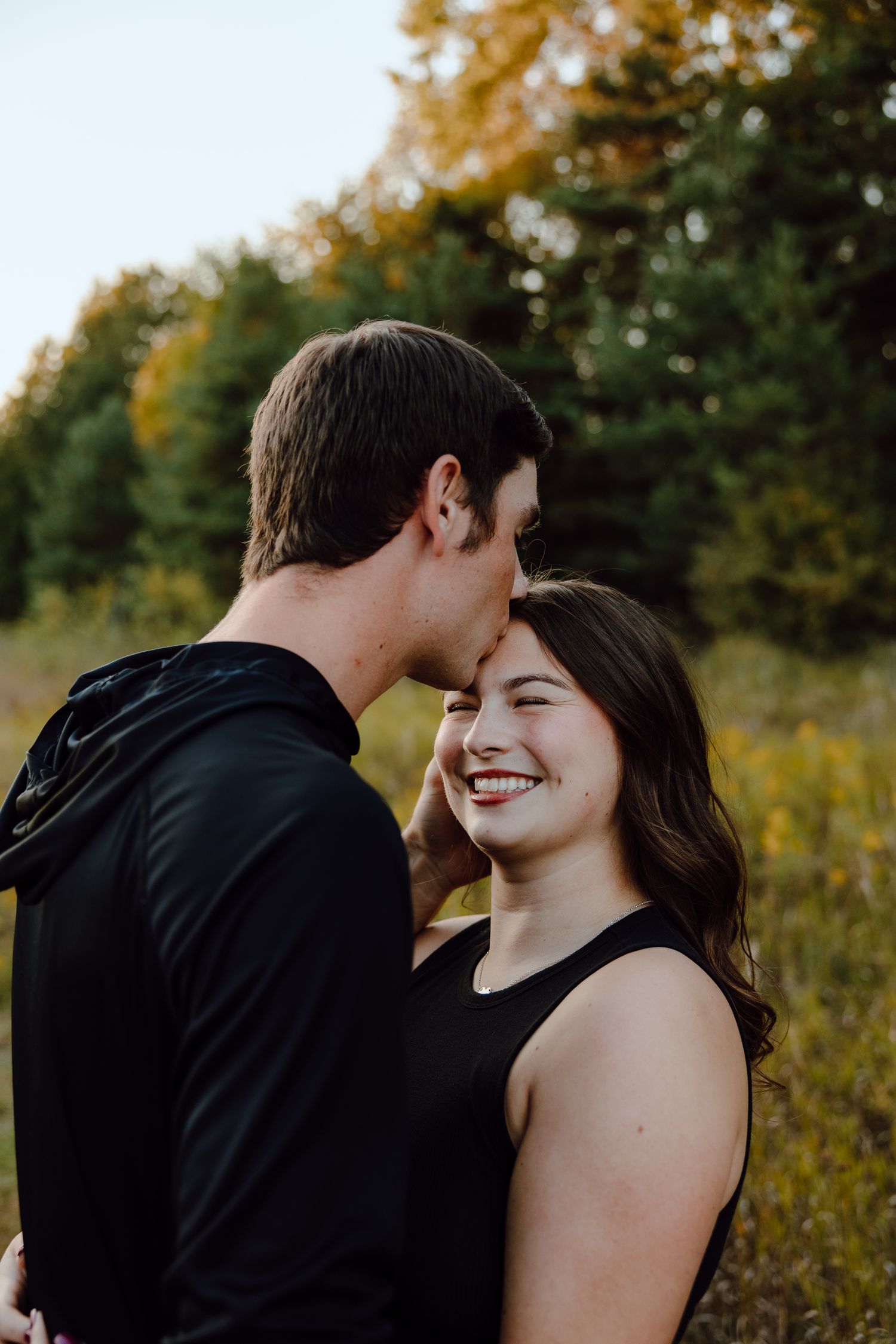A couple shares intimate moments in a sunlit autumn field with golden foliage.