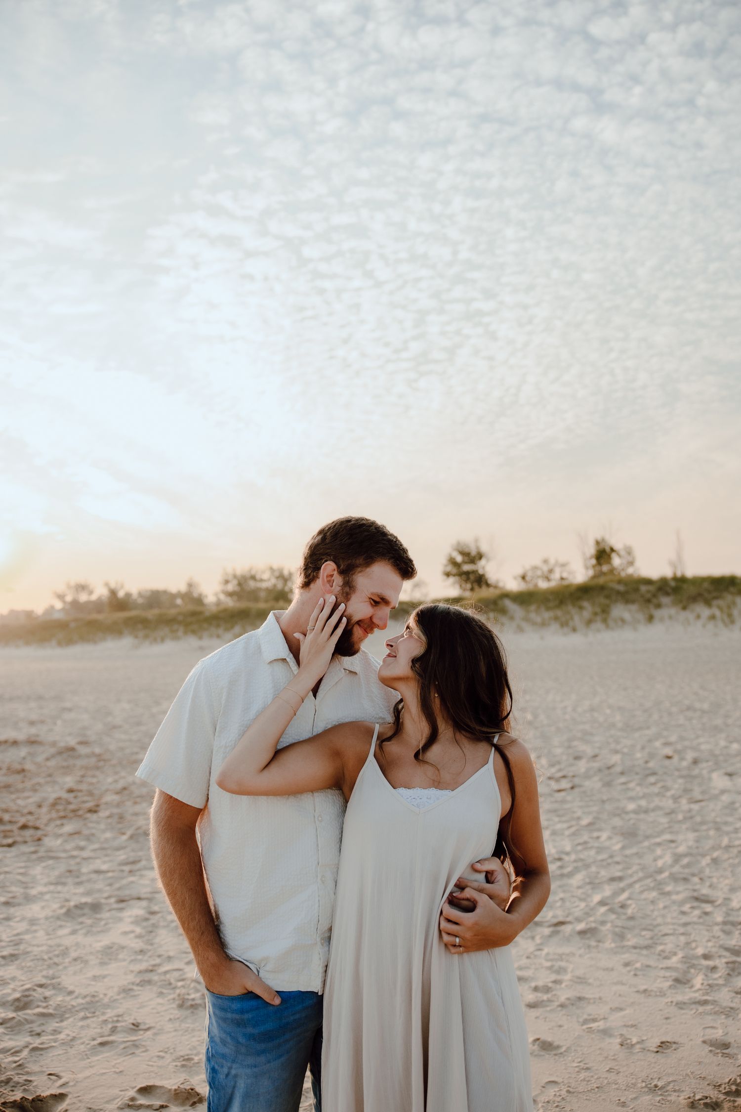 Couple sharing intimate laughs and embraces on a sandy beach during golden hour.