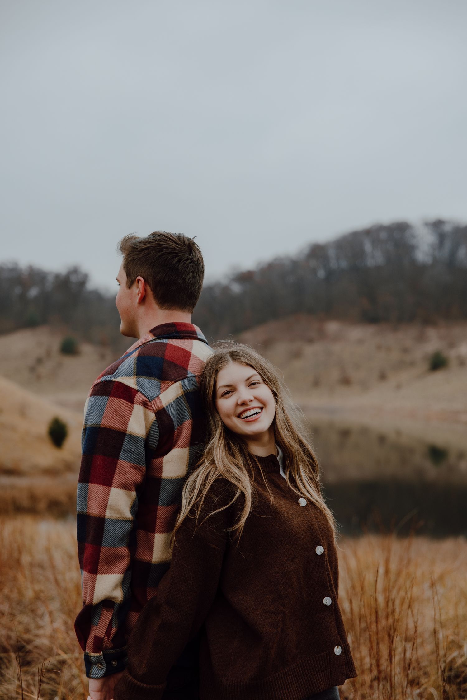 A couple poses together in autumn weather wearing casual outdoor clothing.