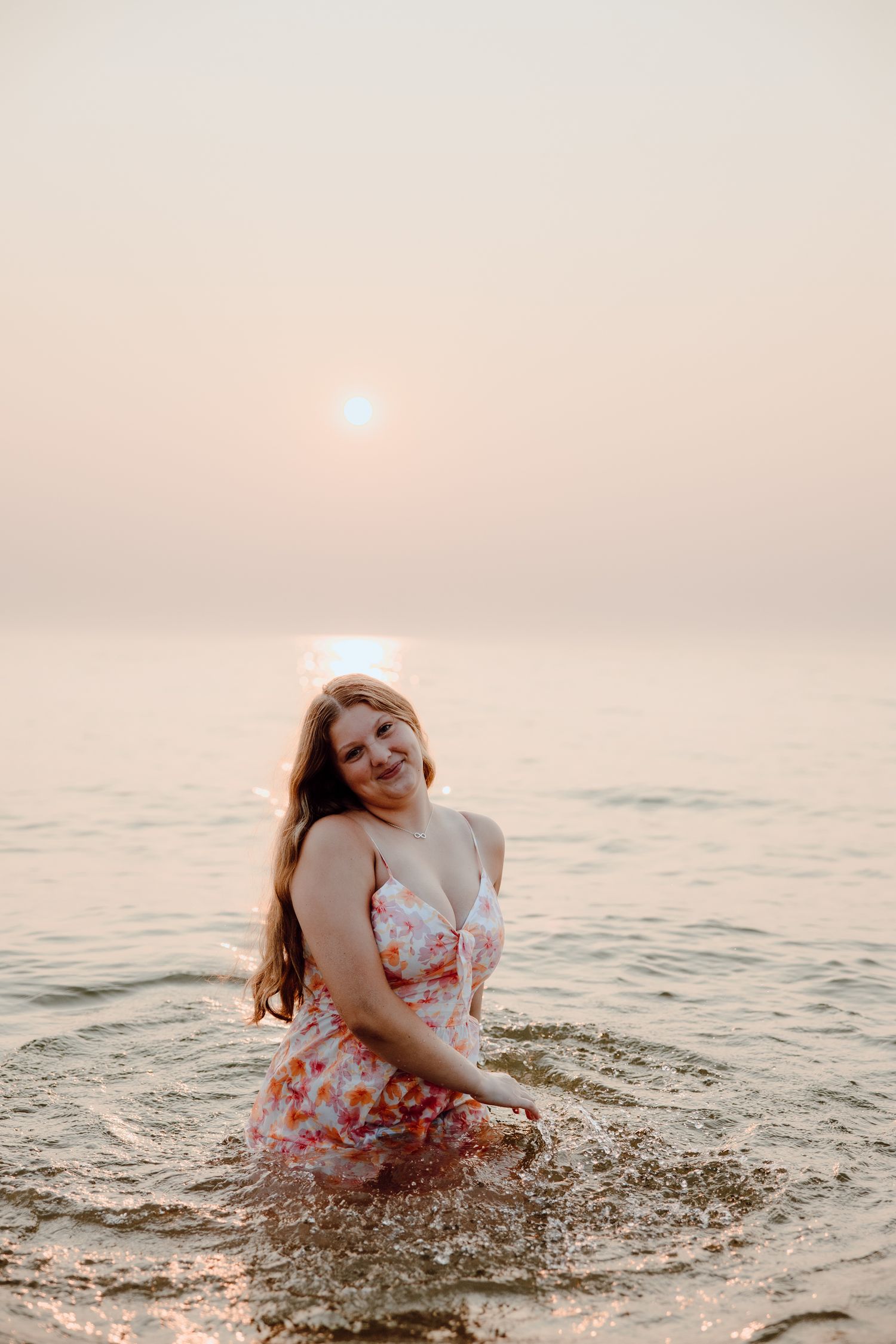 Person in floral sundress splashes in ocean water during golden sunset.