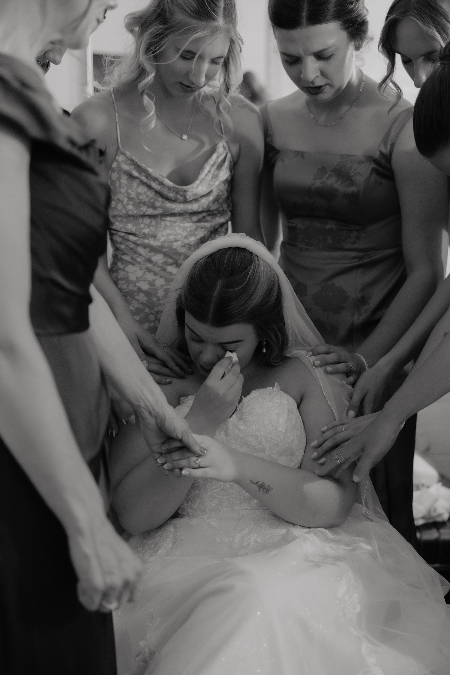 Black and white photo of bridesmaids comforting emotional bride in wedding dress before ceremony.