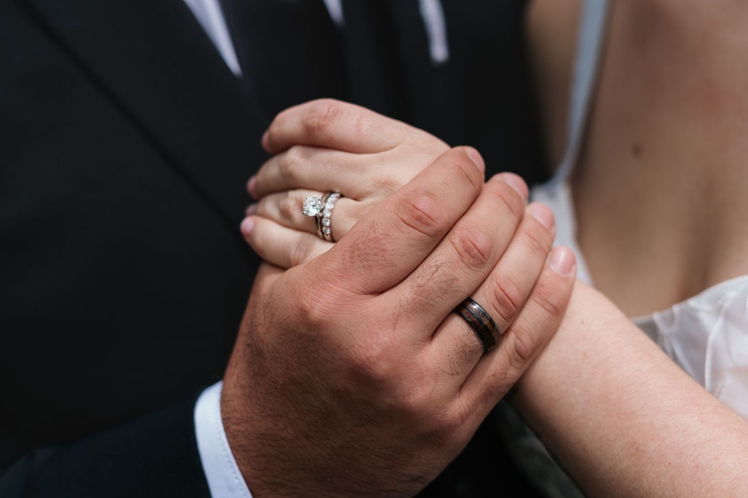 Close-up of newlywed couple holding hands showing wedding rings, bride wearing diamond ring and groom wearing black band.