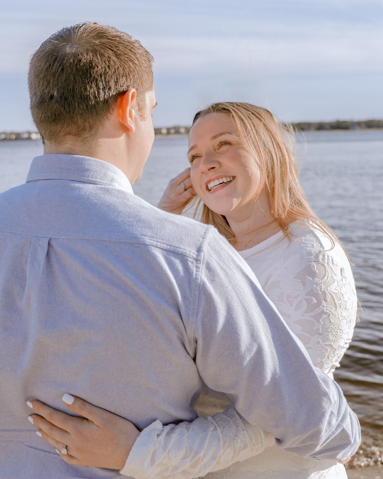 Smiling woman embracing her fiance during a golden hour beach engagement photography session.