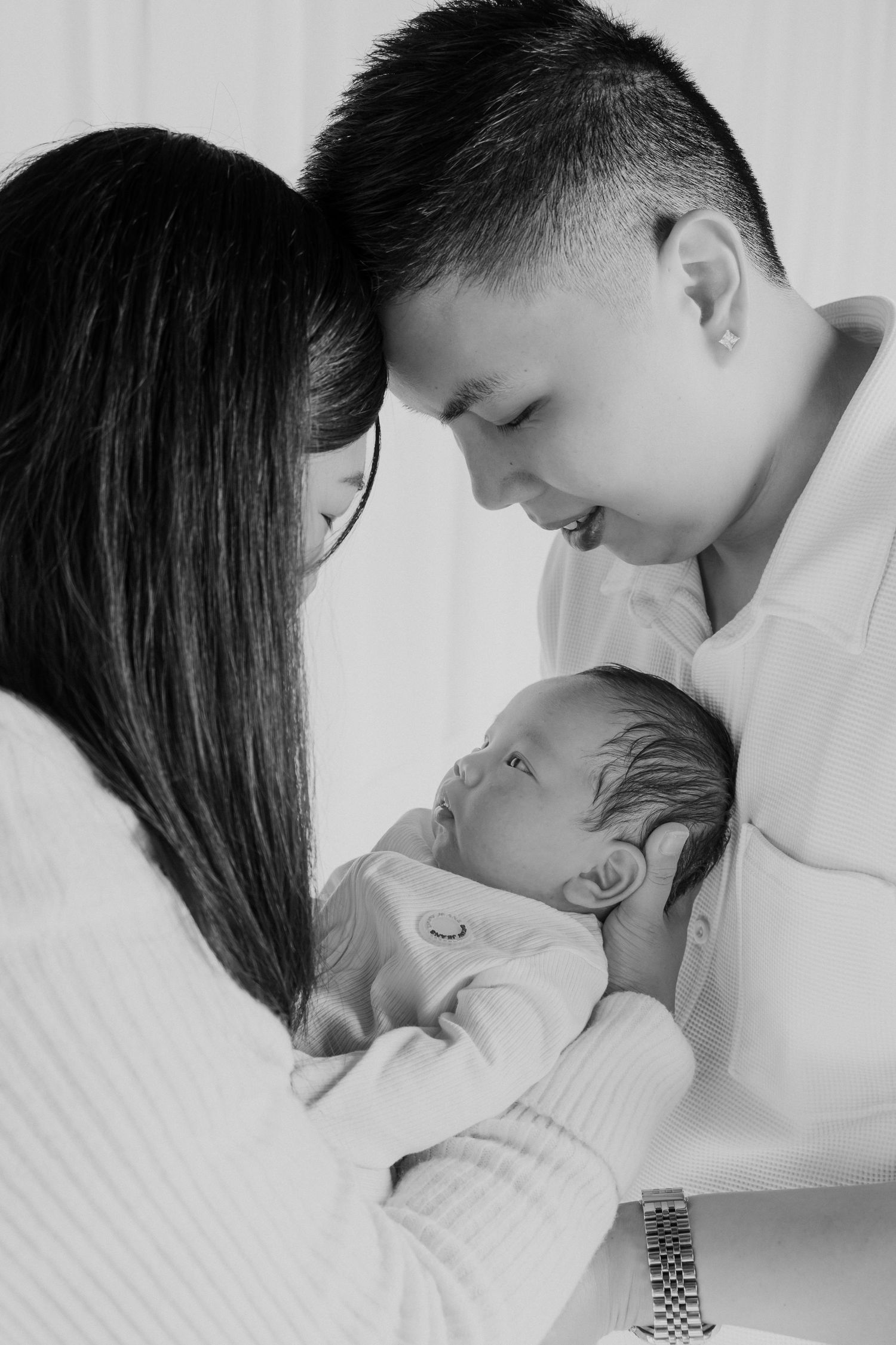 Black and white photo of two parents lovingly holding their newborn baby close together.