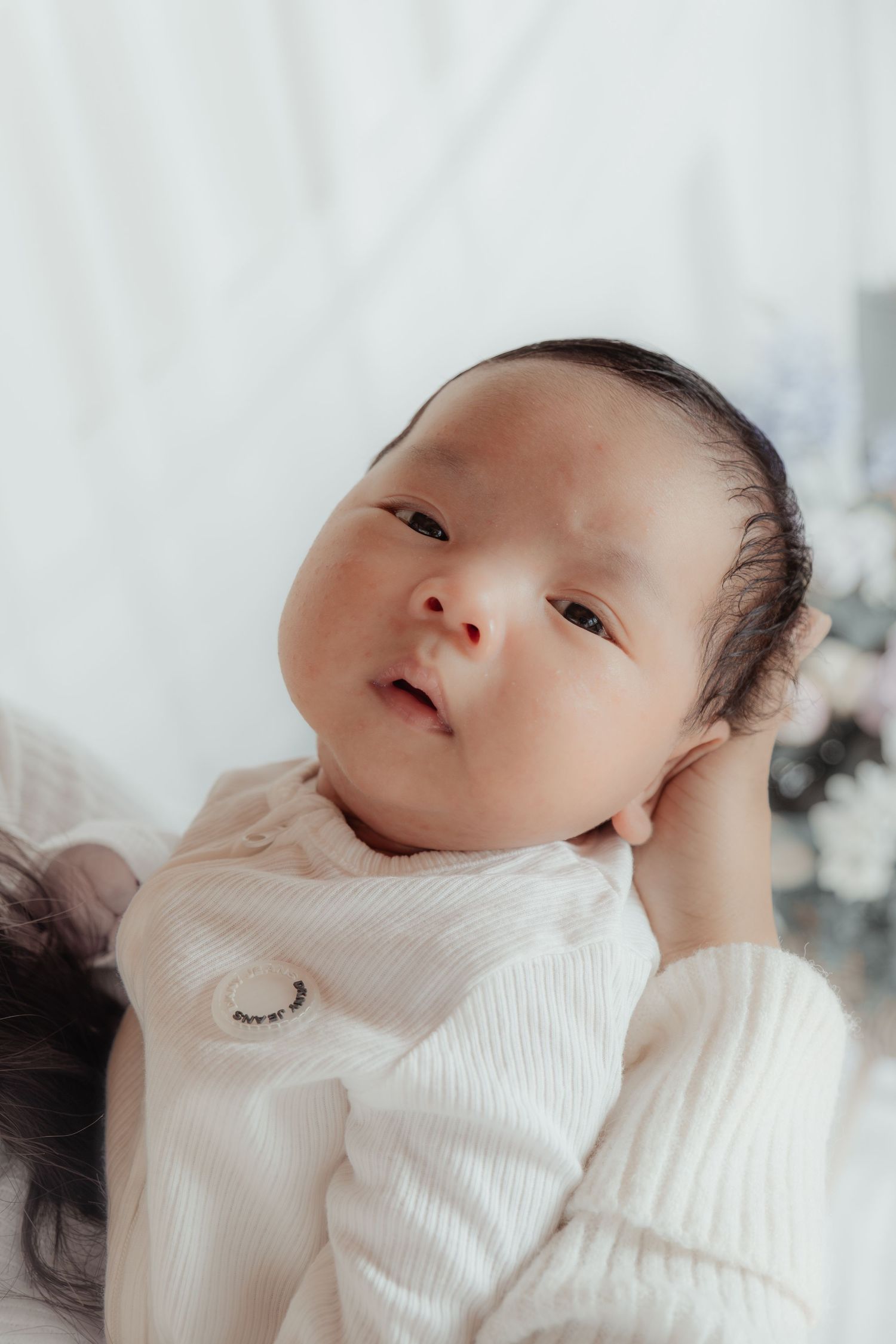 Close-up of a newborn baby in a white ribbed outfit being cradled gently in an adult's hands.