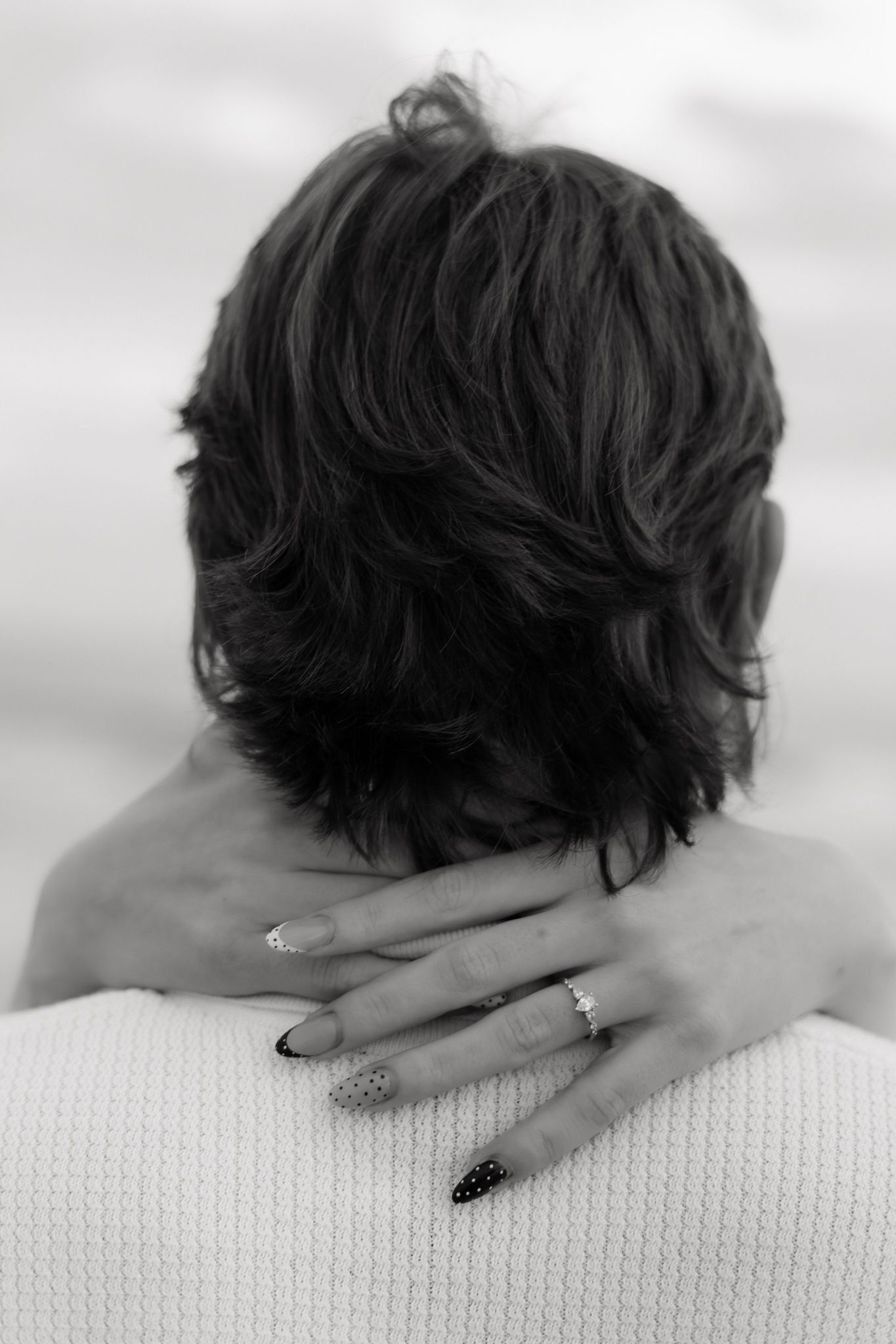 Close-up black and white photo of a woman with short hair, hand resting on a mans shoulder wearing a ring.