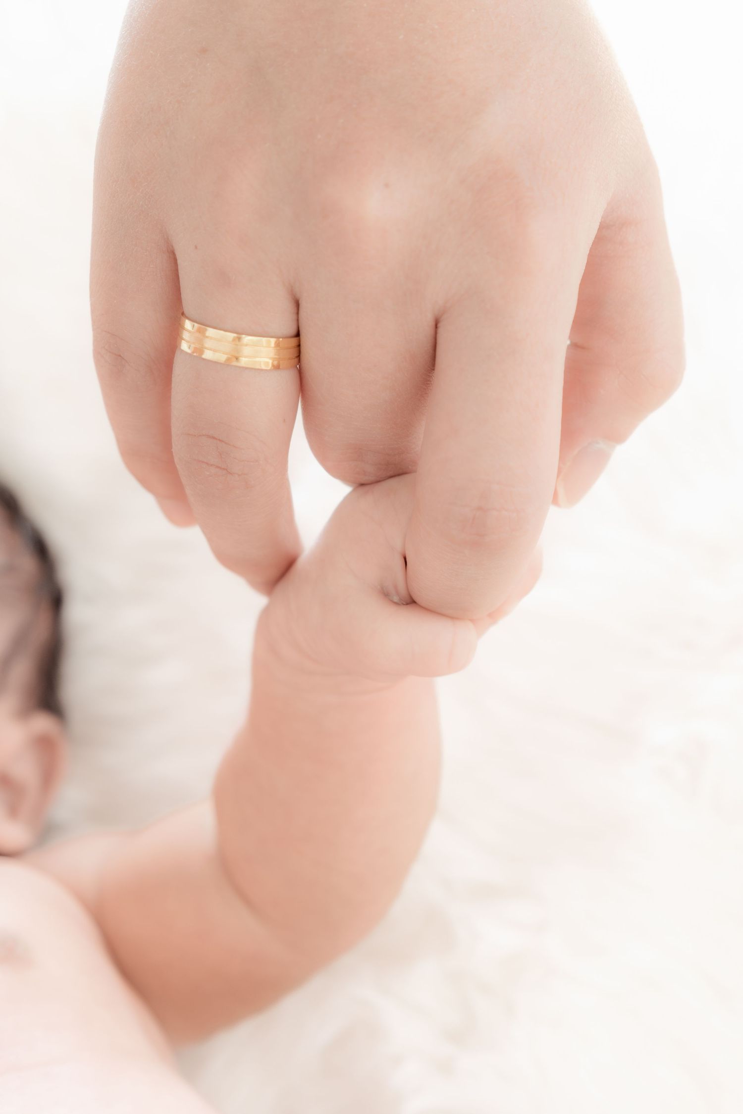 A newborn baby grasping an adult finger wearing a gold ring, symbolizing family love and new parenthood.