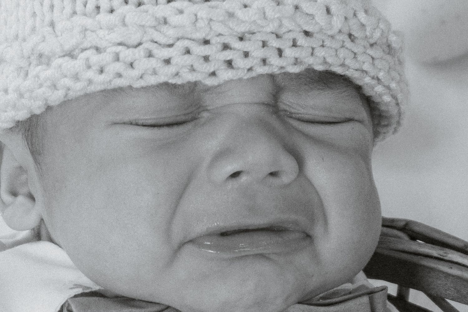 A close-up black and white portrait of a newborn baby wearing a knit hat.