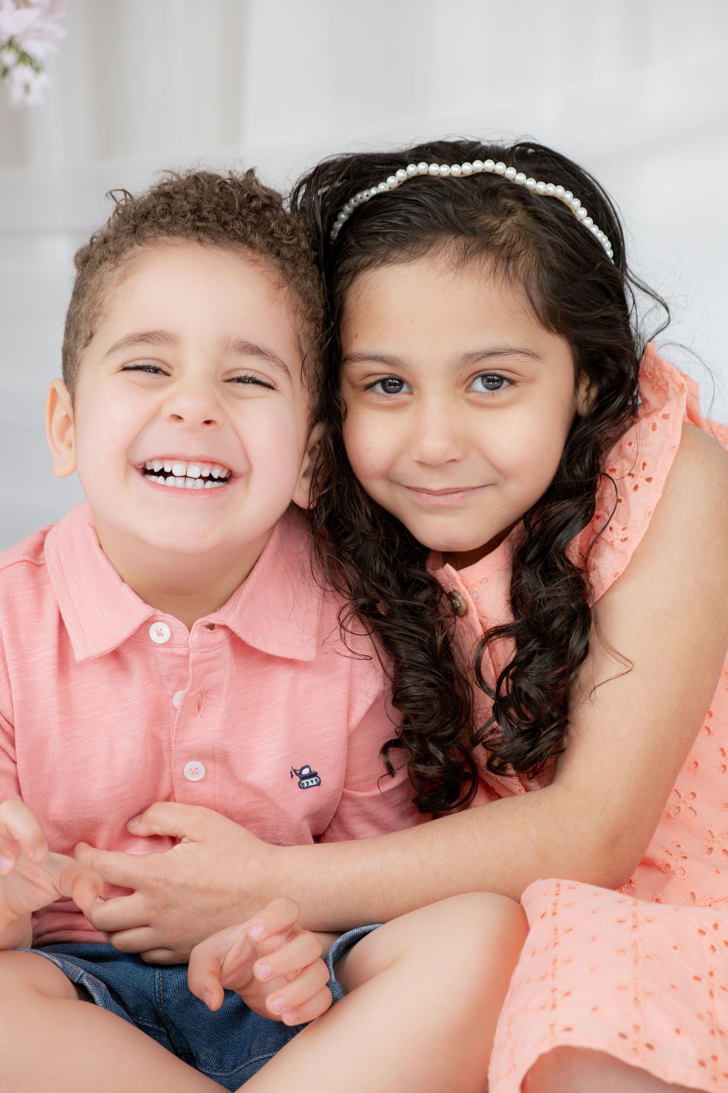 Two smiling children in pink outfits pose together in a bright white studio photo session.