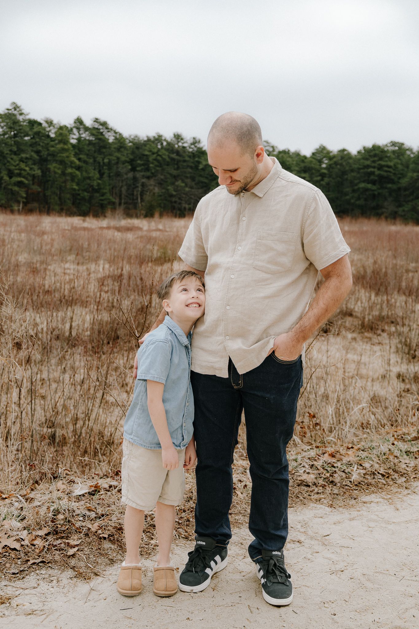 A father and young son share a sweet moment together on a sandy path in a field.
