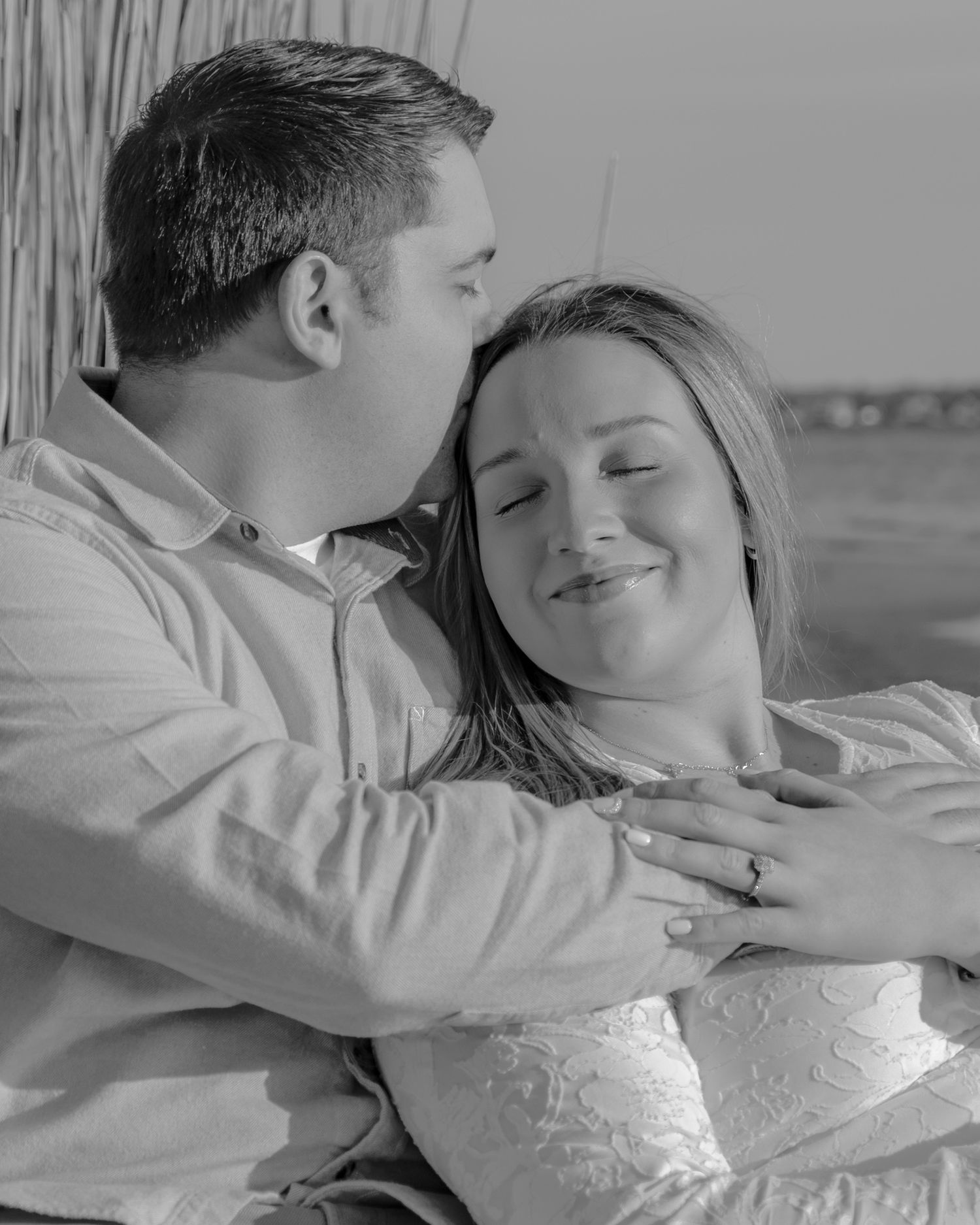 Black and white romantic photo of couple embracing, man kissing woman's cheek as she smiles with eyes closed.