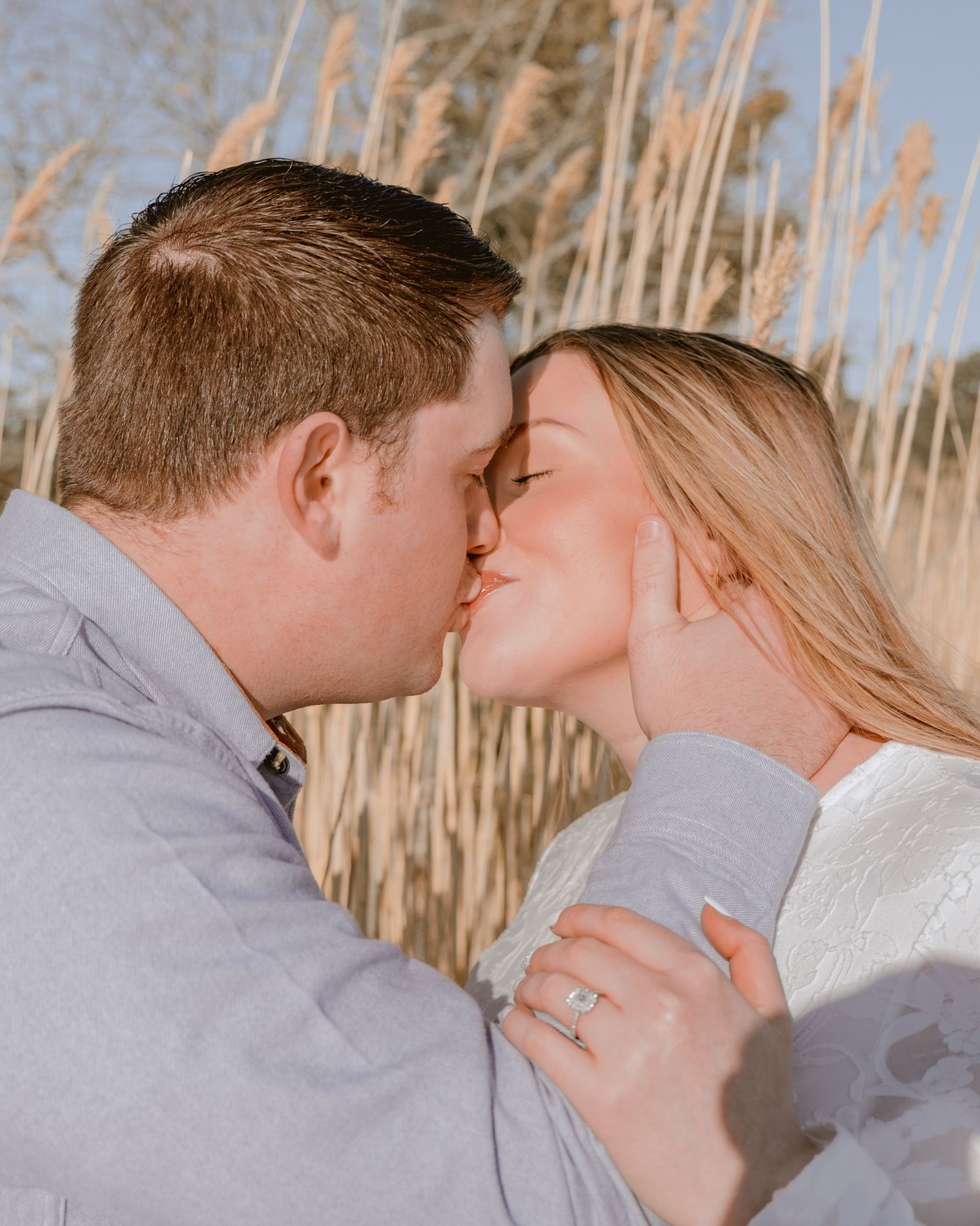 Couple sharing a romantic kiss in front of golden beach grass during engagement photo session.