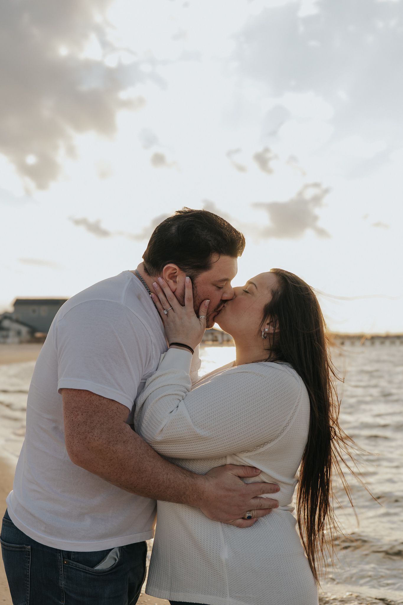 Couple sharing a romantic kiss on the beach at sunset, embracing each other near the ocean shore.