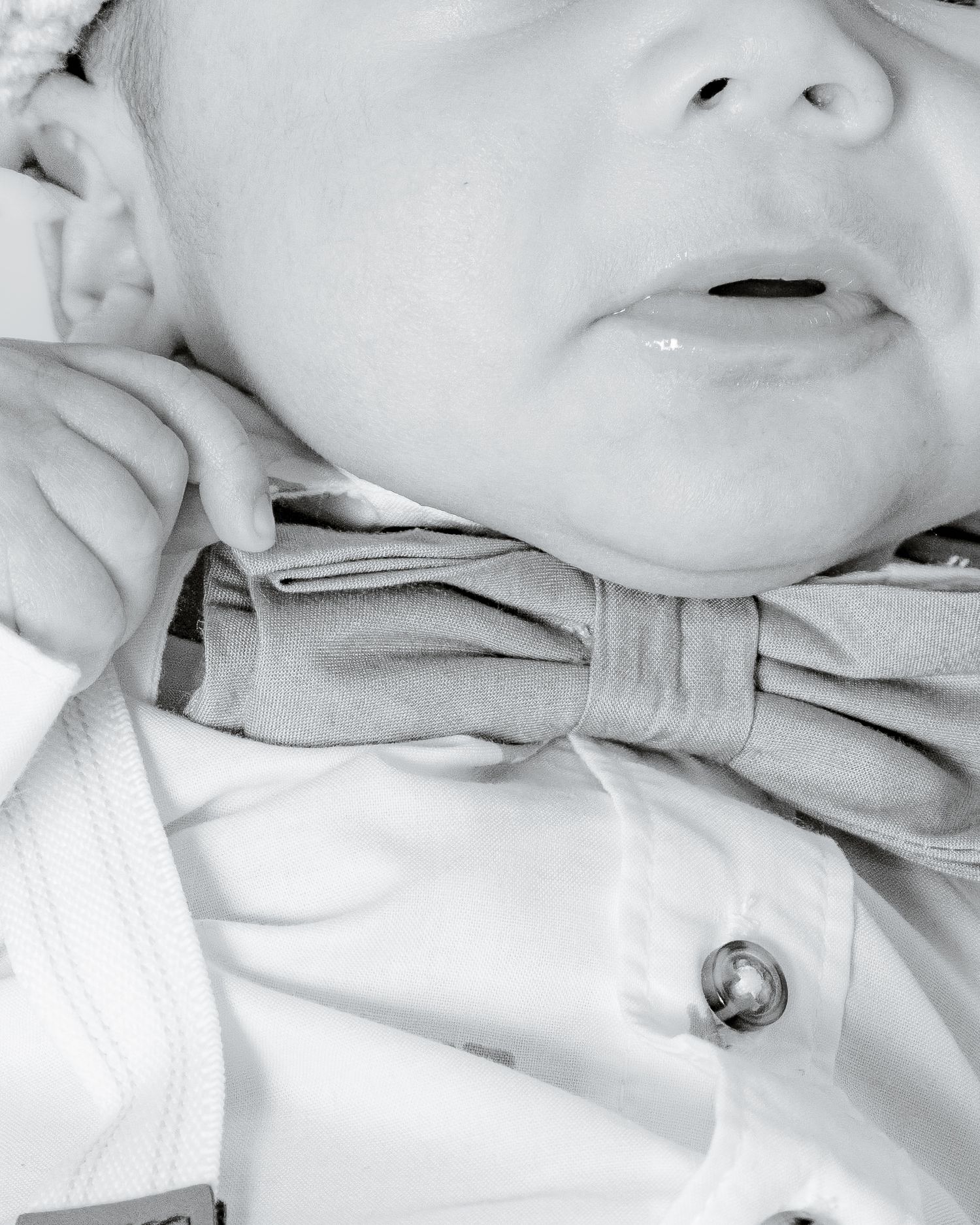 Close-up black and white photo of a newborn baby wearing a bow tie outfit.