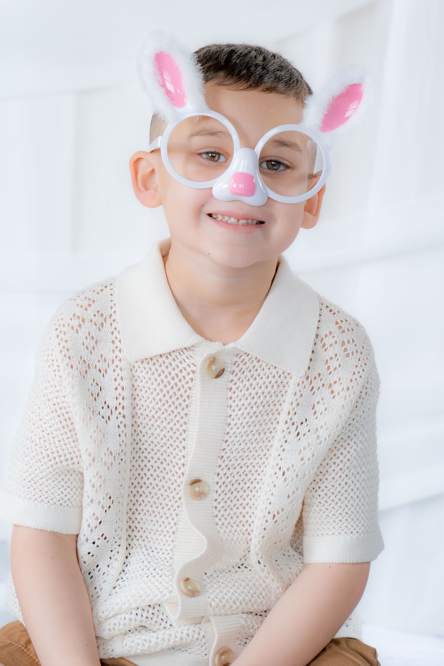 Smiling boy wearing novelty Easter bunny face glasses and white knit shirt.