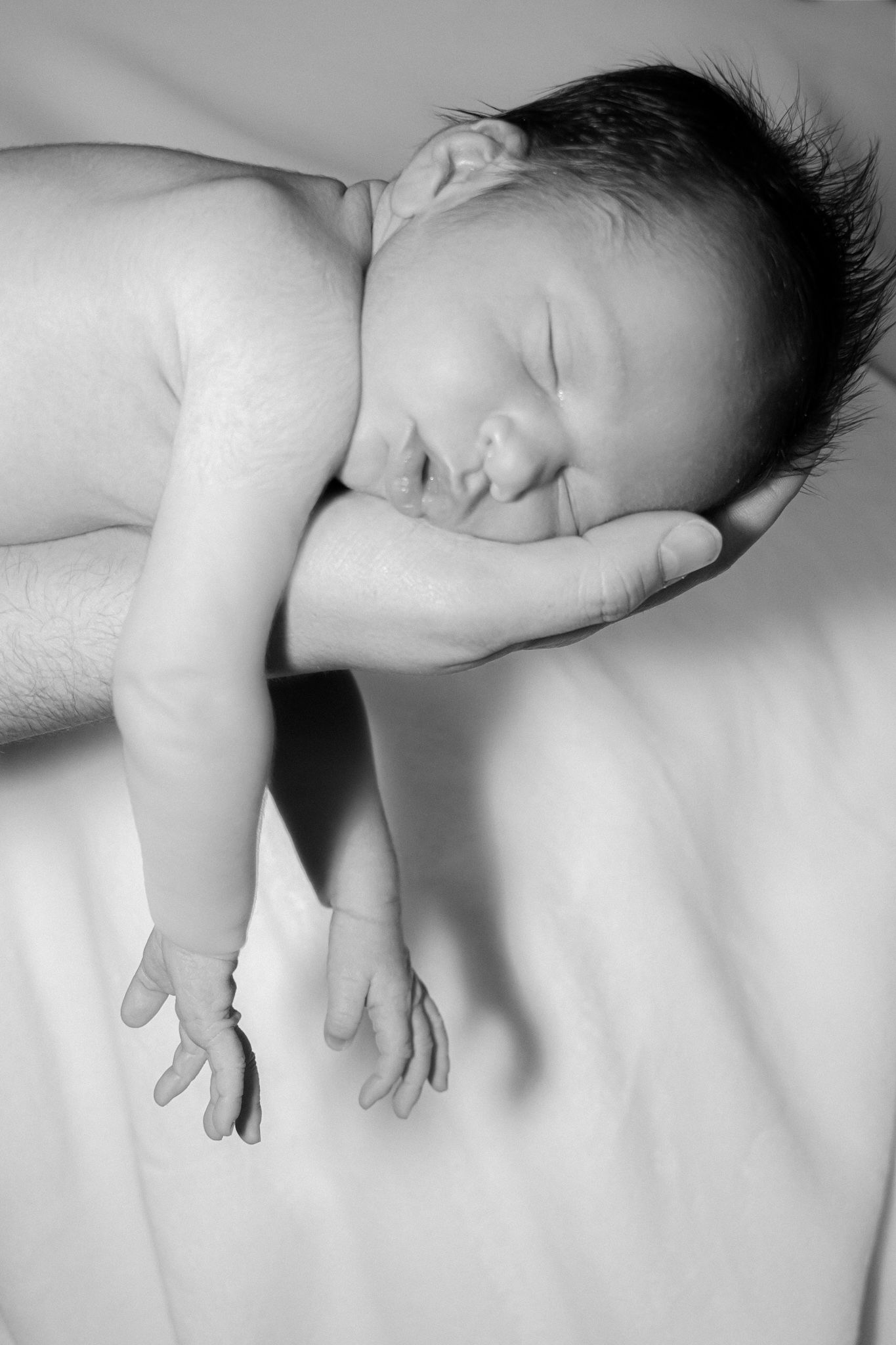 Serene newborn baby sleeping peacefully on a parents hand in black and white photo.