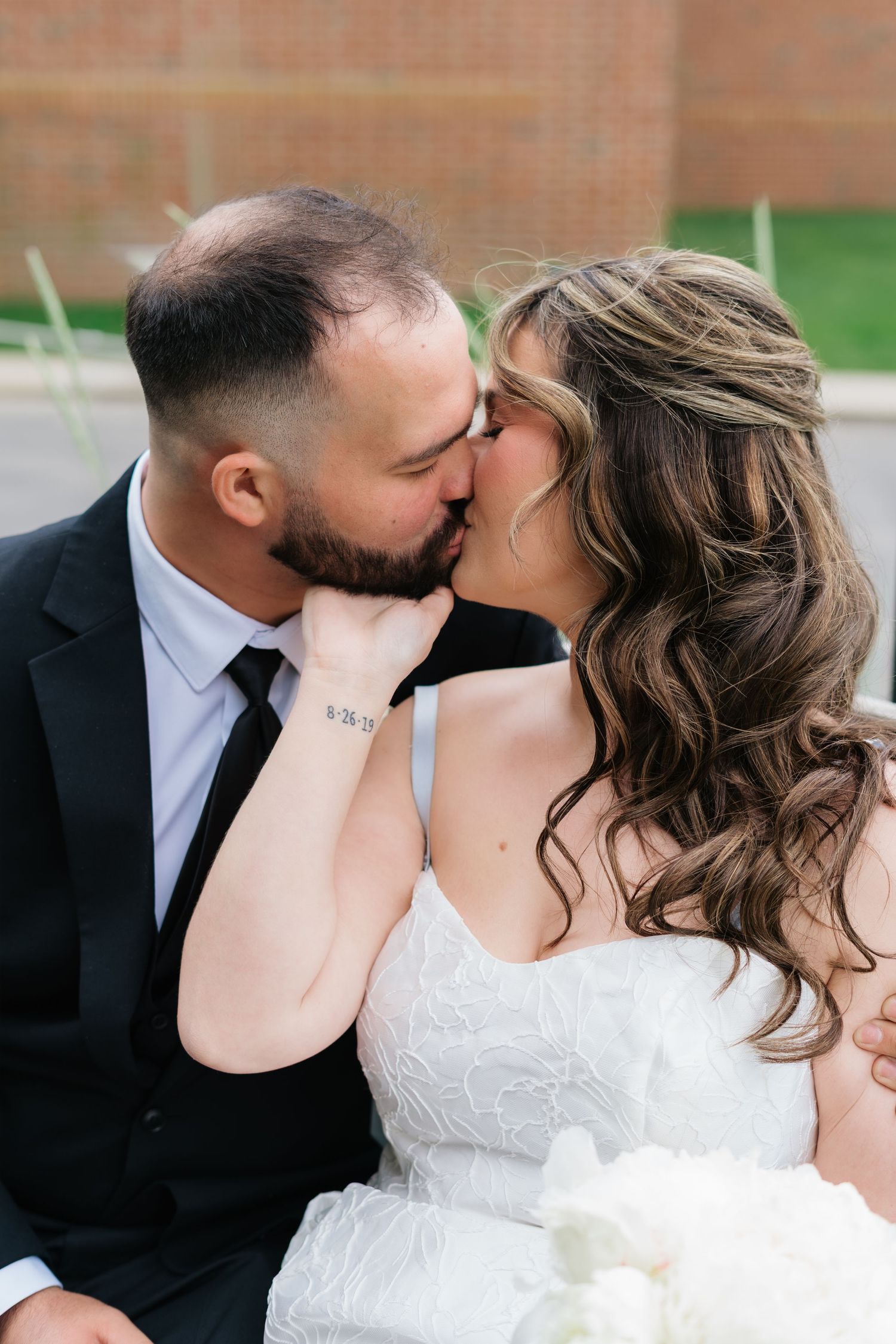 Bride and groom share a romantic kiss on their wedding day, bride in white lace gown holding grooms face tenderly.