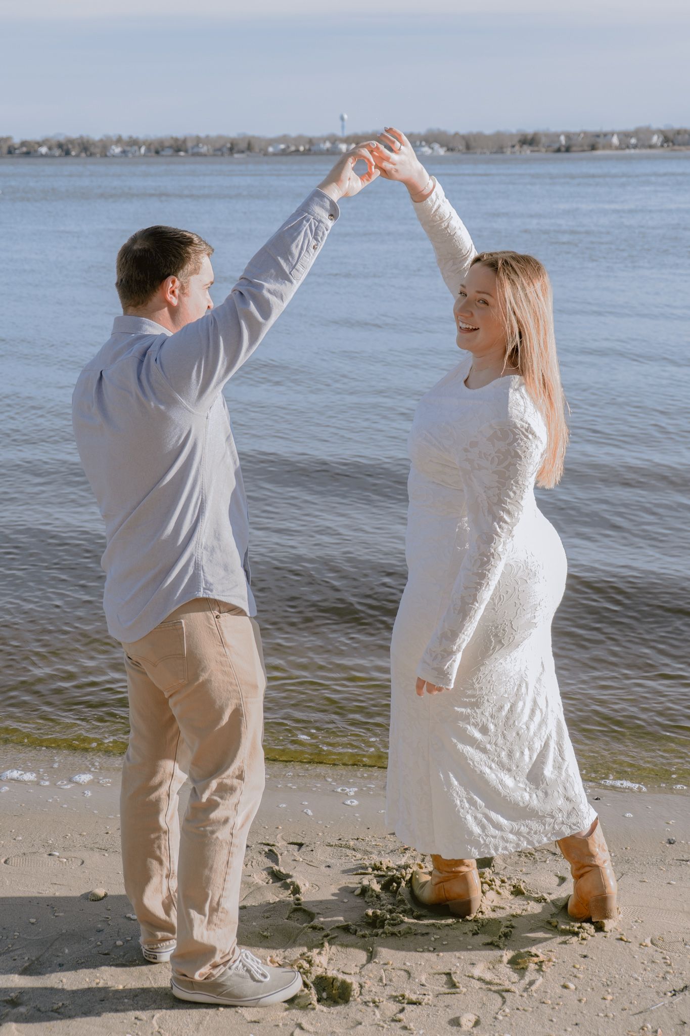 Joyful engaged couple dancing and spinning on the beach with ocean water in the background.