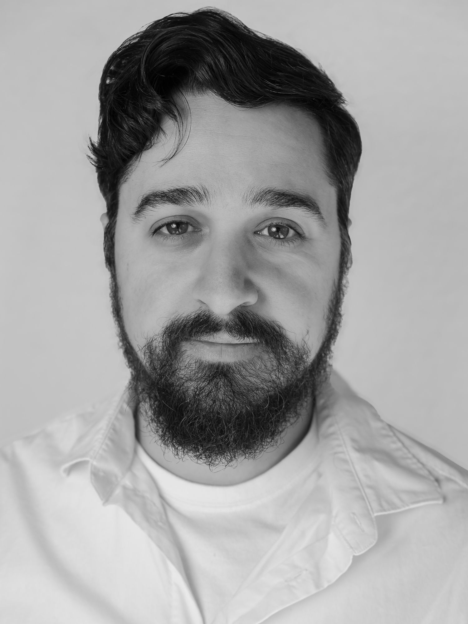 Black and white professional headshot of a bearded man with dark hair wearing a white shirt.