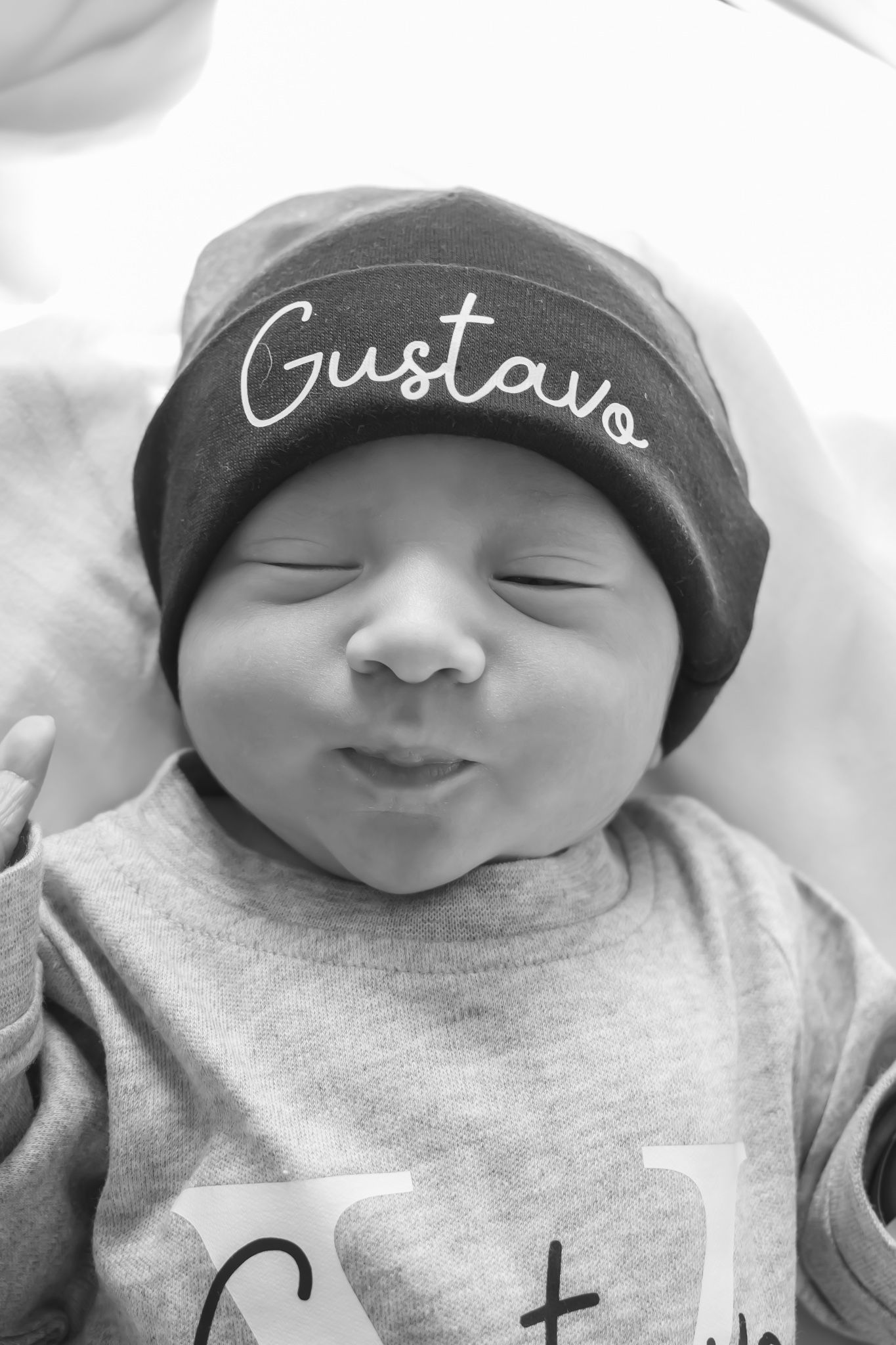 Sleeping newborn baby wearing a personalized hat with the name Gustavo in black and white.