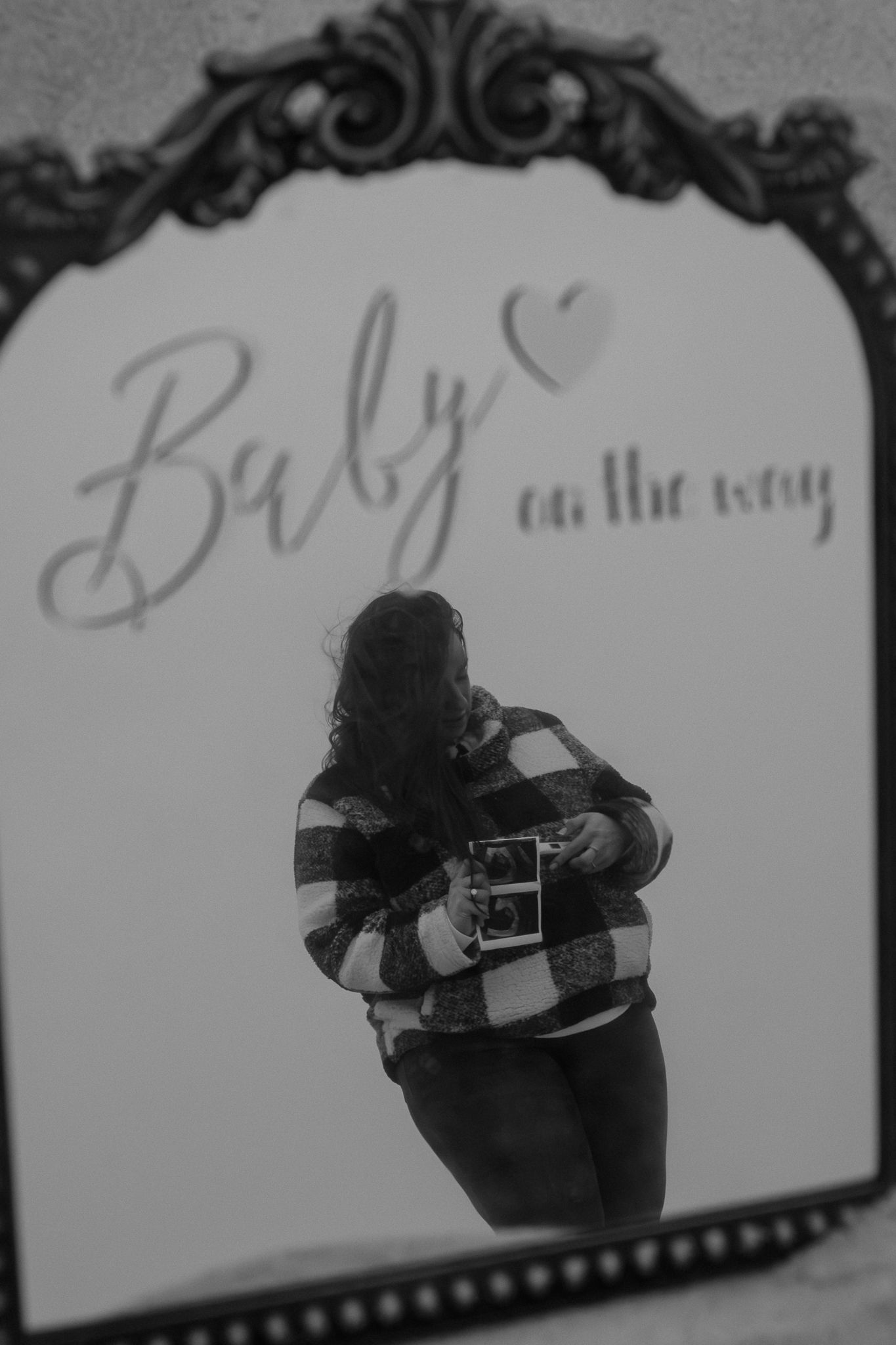Black and white mirror selfie of pregnant woman holding ultrasound photo with Baby on the Way text.