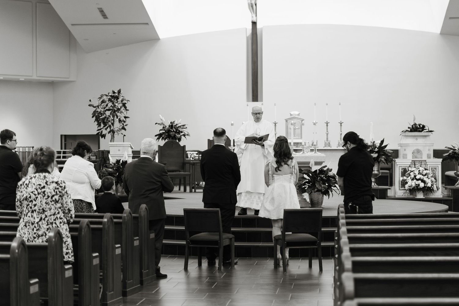Wedding ceremony inside a church with guests standing at the altar before a priest.