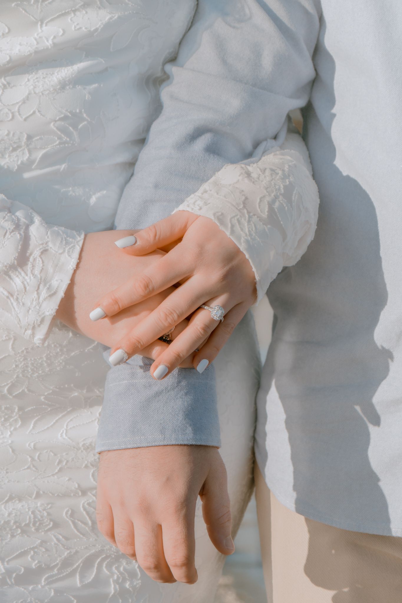 Close-up of engaged couple holding hands showing off a stunning diamond halo engagement ring.