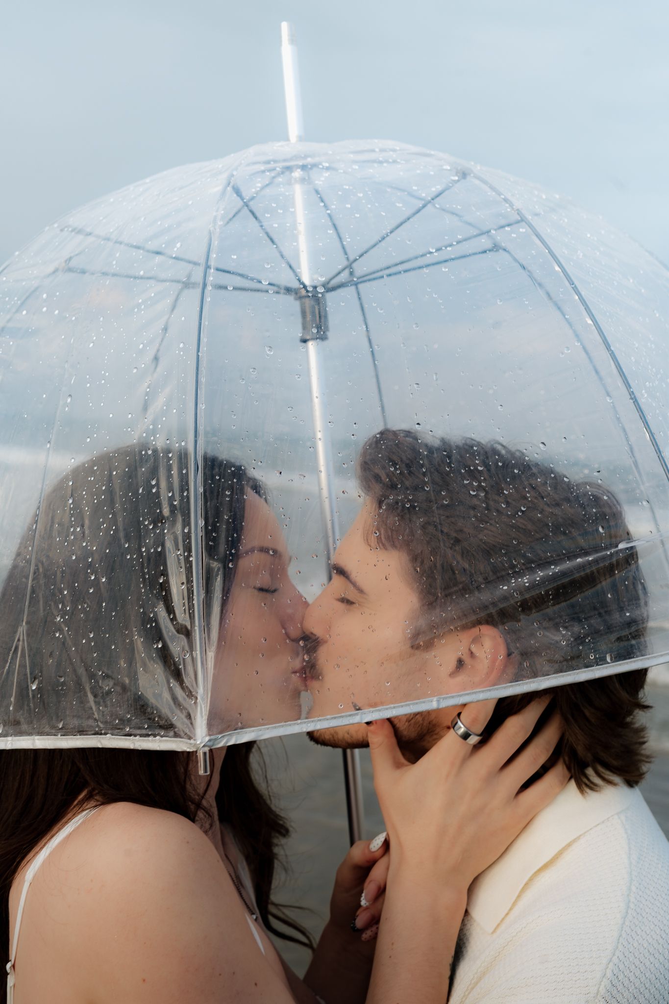 Couple sharing a romantic kiss under a clear transparent umbrella in the rain.