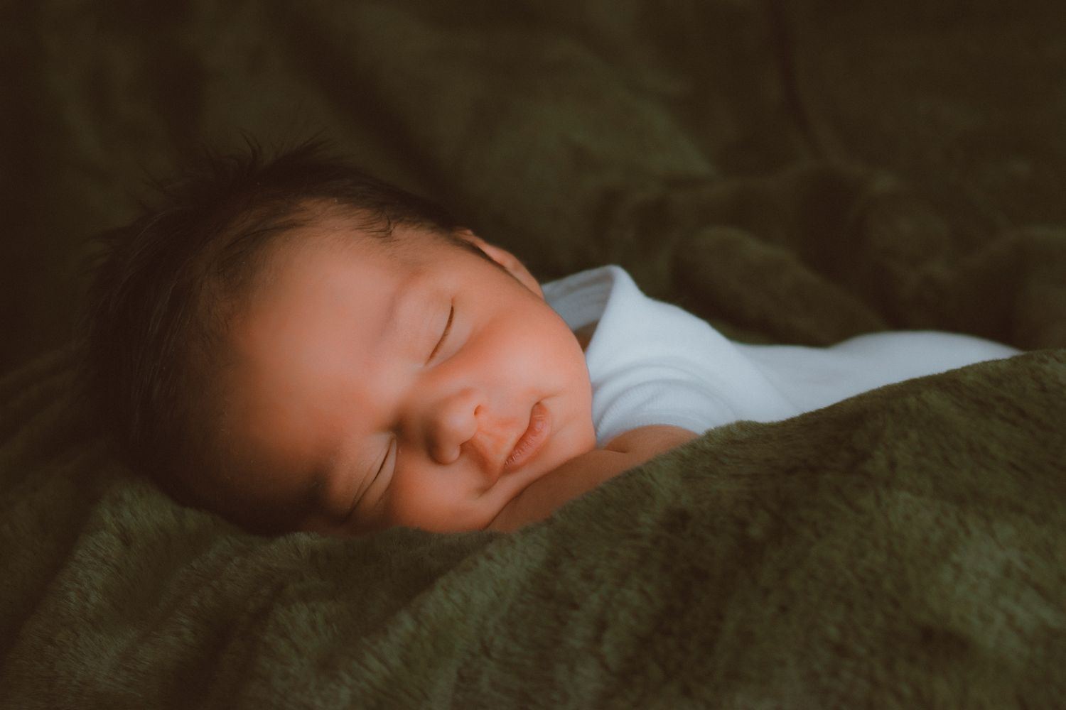 Peaceful newborn baby sleeping swaddled in white wrap on a soft dark green blanket.
