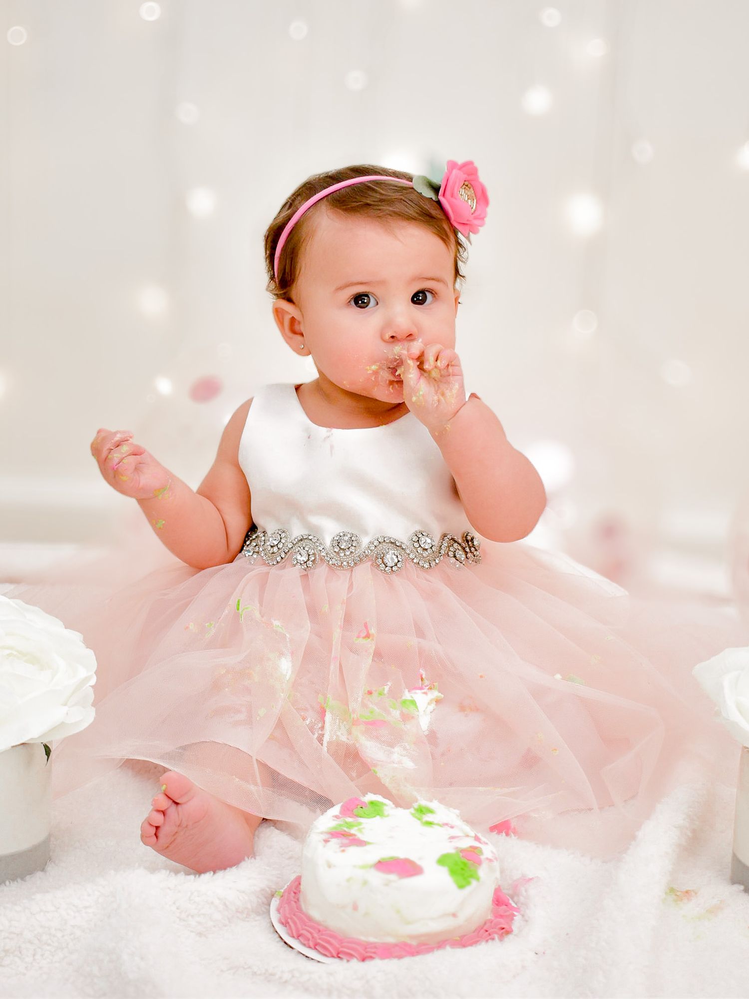 Baby girl in pink tutu dress eating her first birthday cake smash indoors.