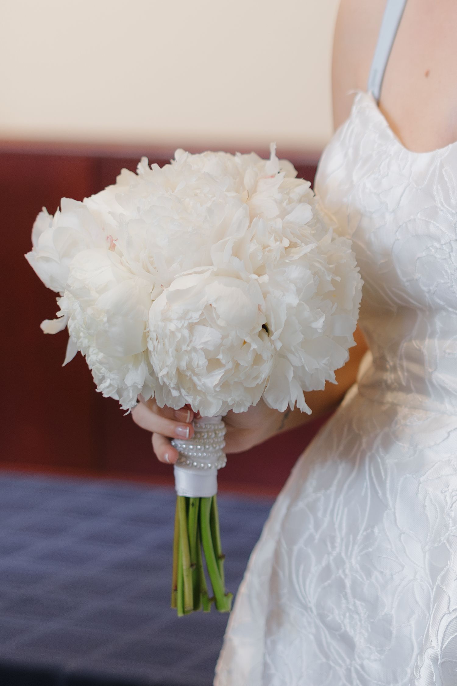 Bride holding a lush round bouquet of white peonies wrapped with pearl-accented ribbon on her wedding day.