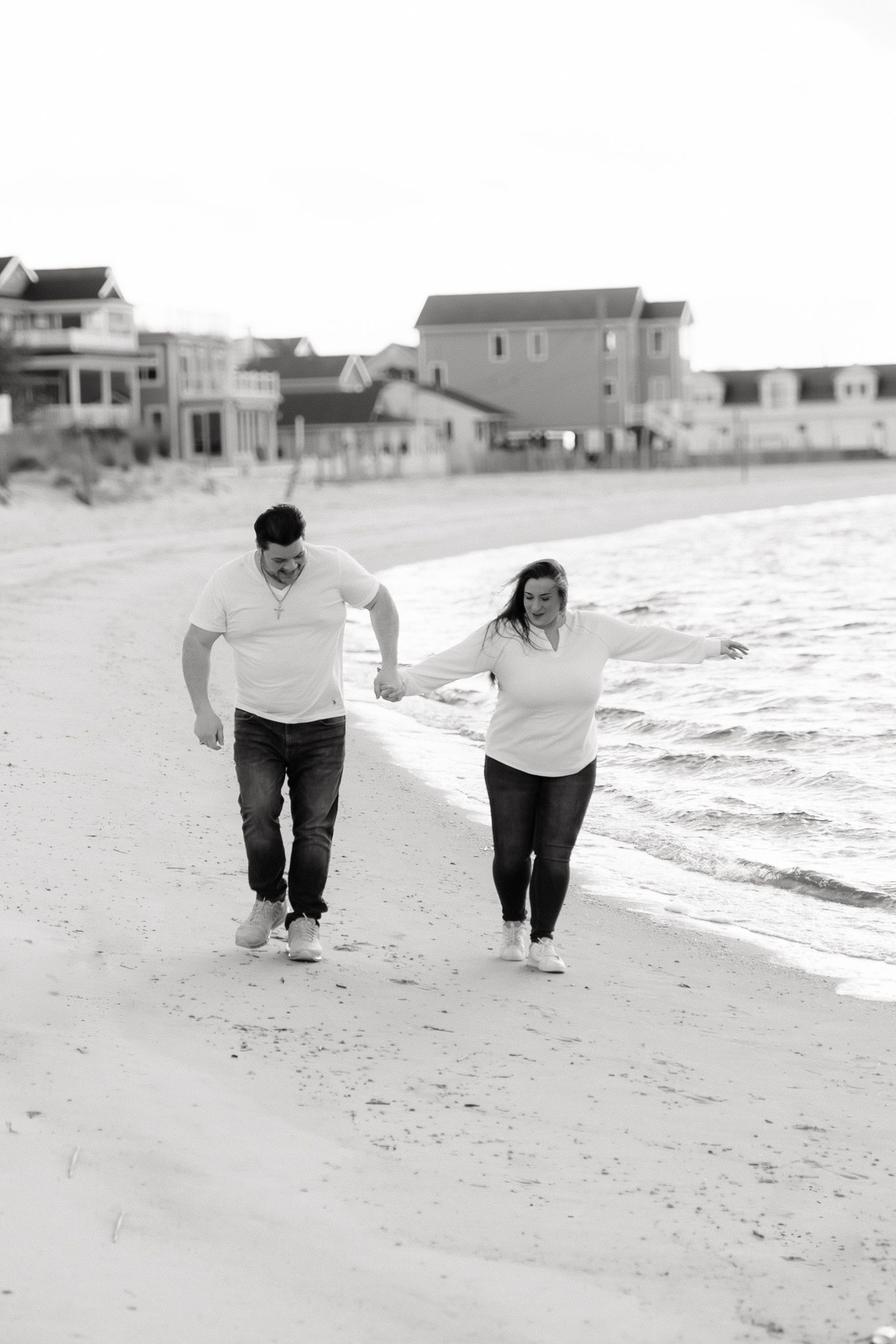 Couple holding hands and walking along sandy beach in black and white photo.