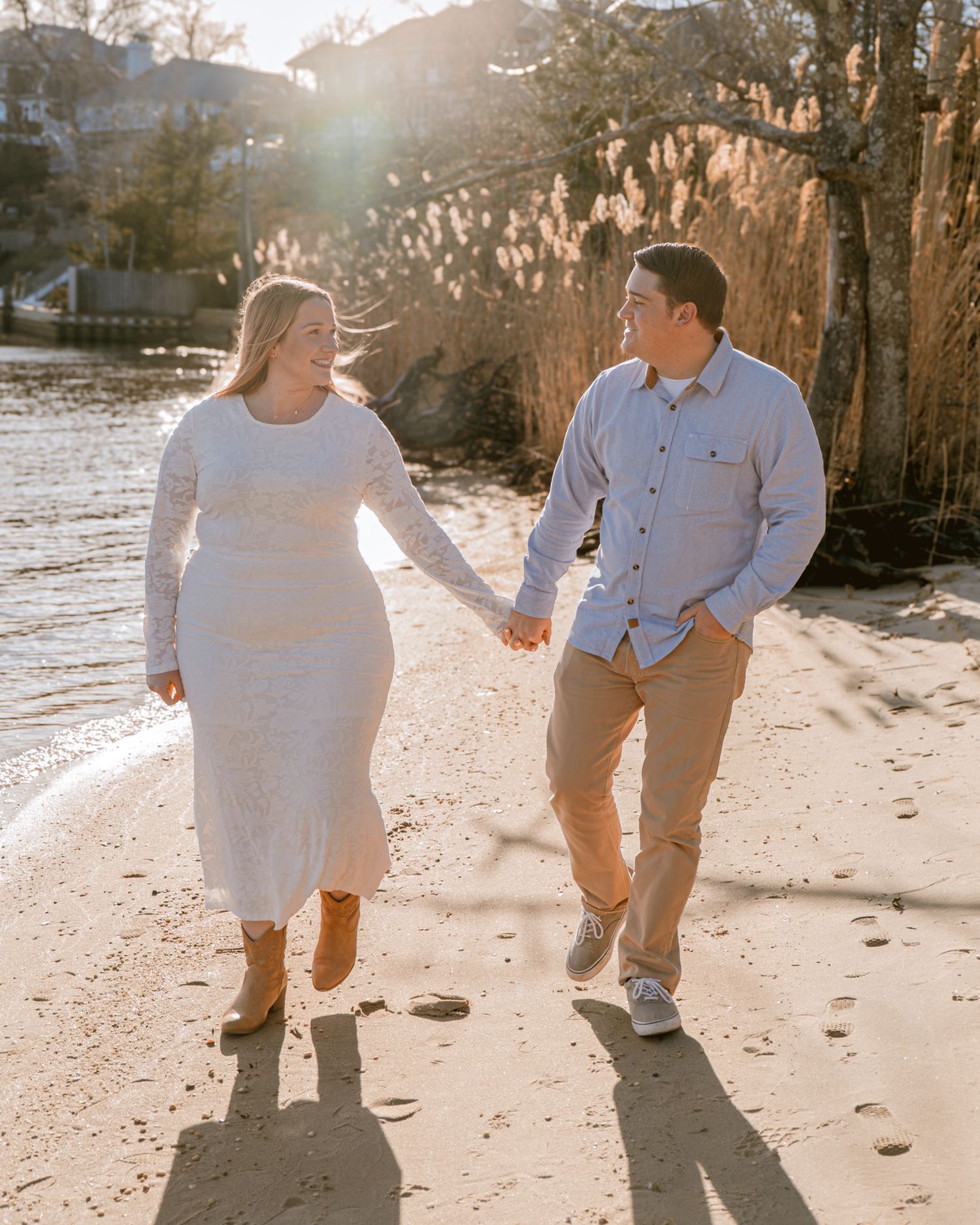 Joyful couple holding hands and walking along a sandy beach at golden hour sunset.