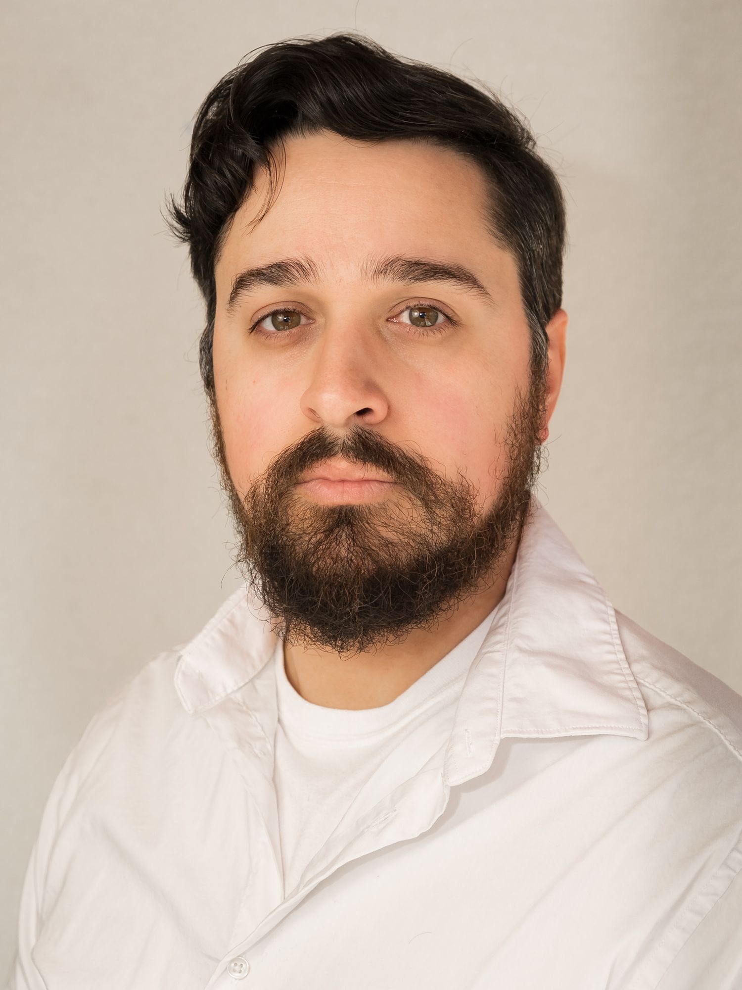 Professional studio headshot of a dark-haired bearded man in a white shirt on a neutral background.