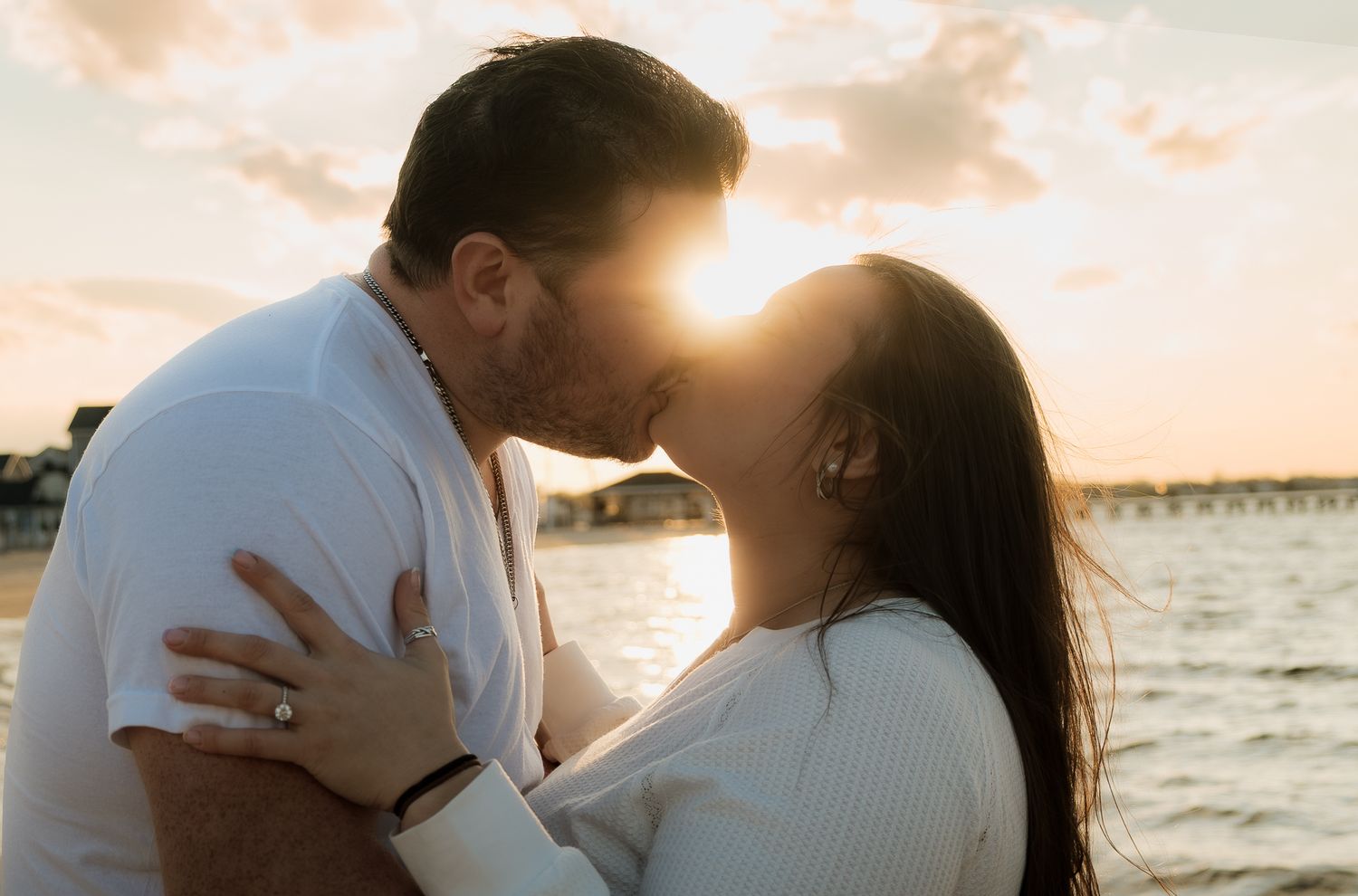 Couple sharing a romantic kiss at sunset by the water, with golden light glowing behind them on a beautiful evening.