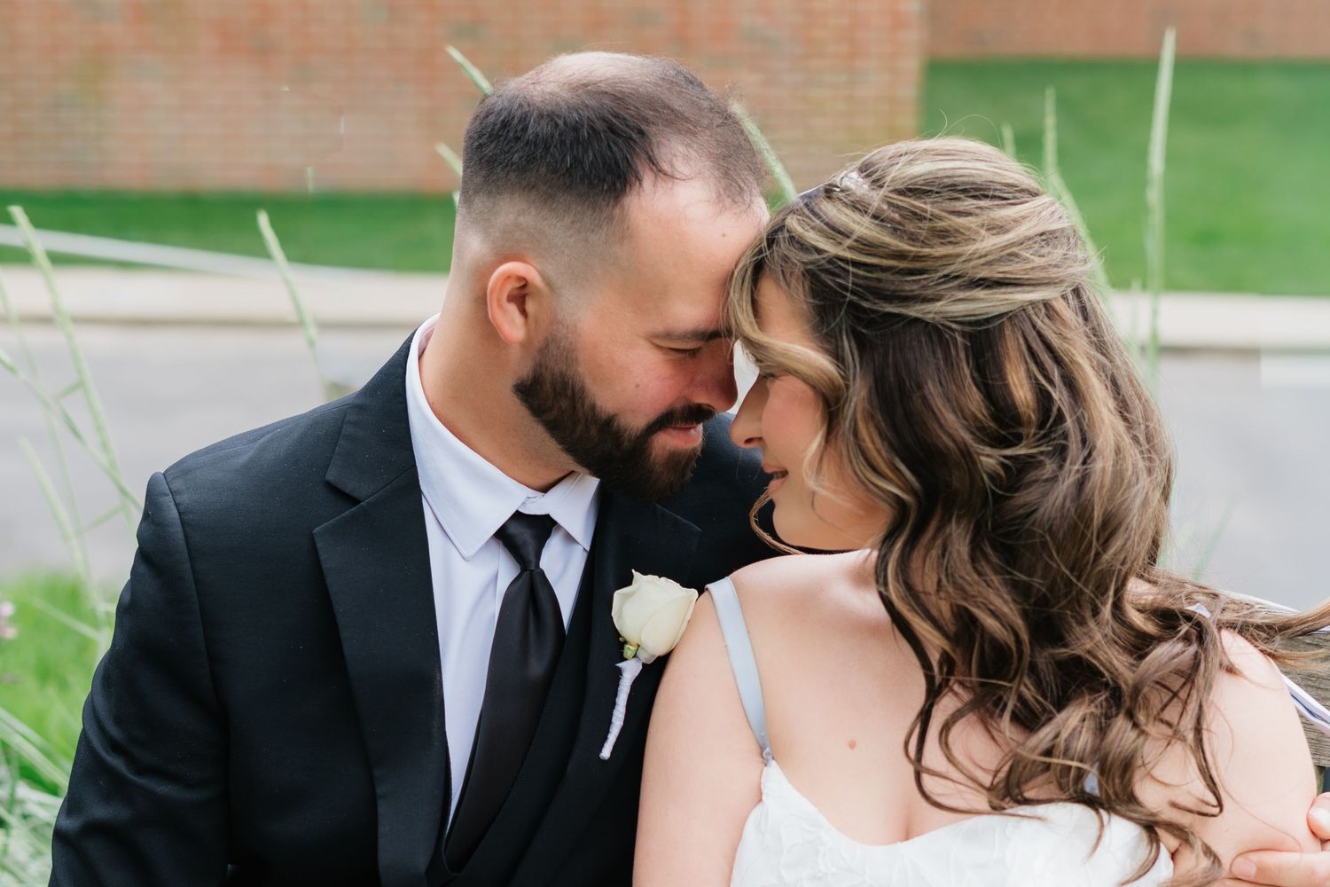Bride and groom sharing an intimate forehead touch moment, groom in black suit with white boutonniere.