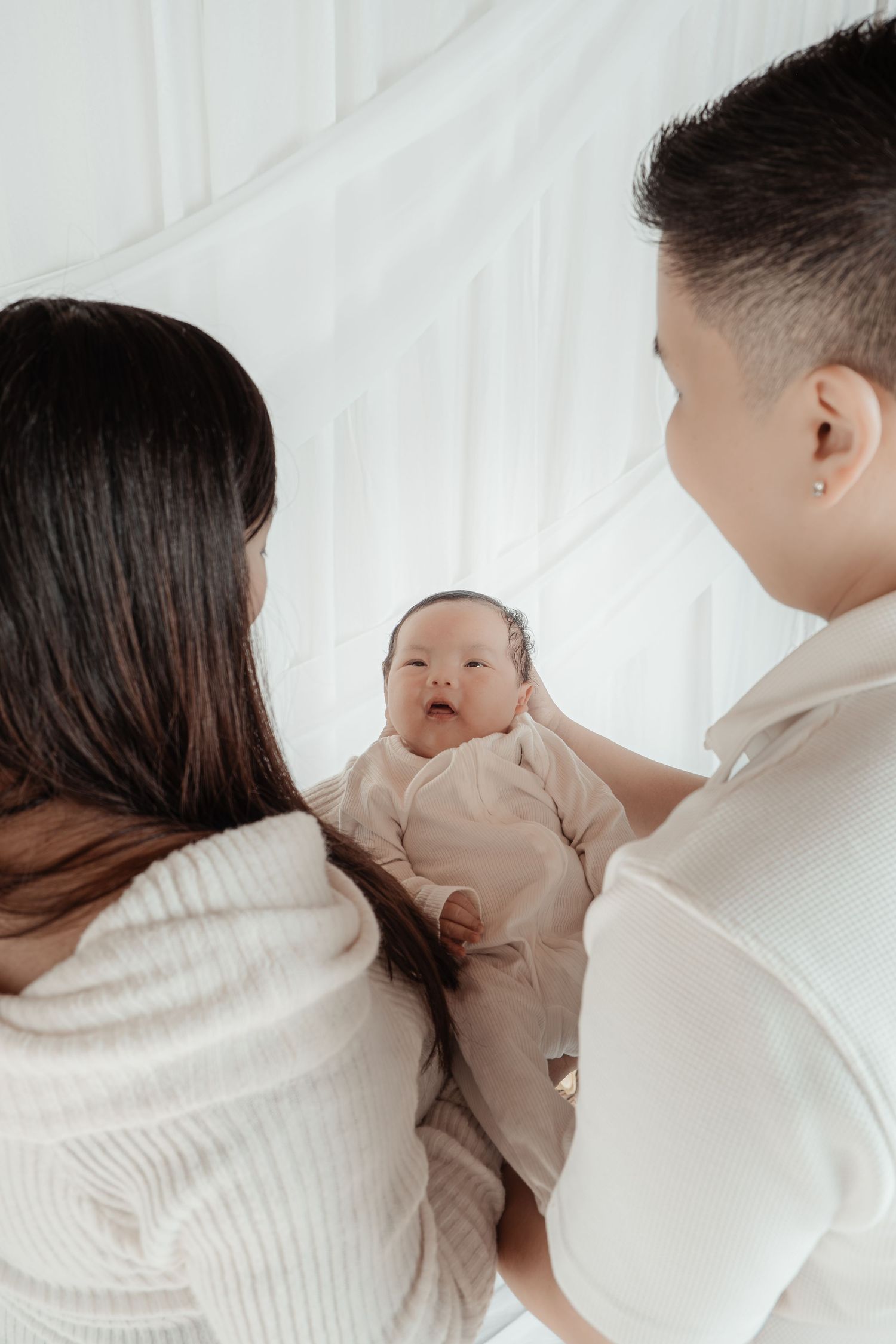 Two parents holding their newborn baby dressed in pink, sharing a tender family moment against a white background.