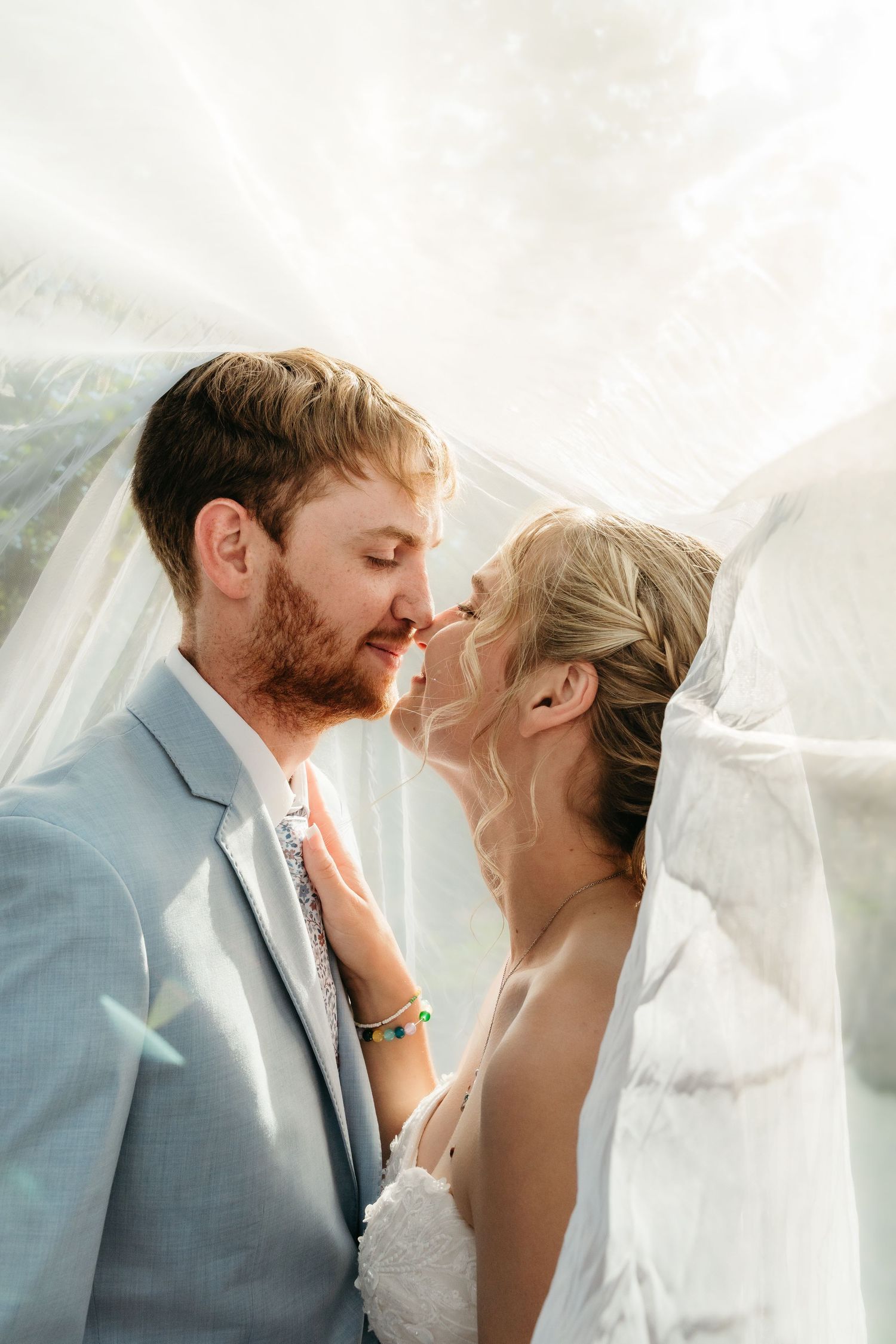 Bride and groom sharing romantic moment under flowing white veil on wedding day.