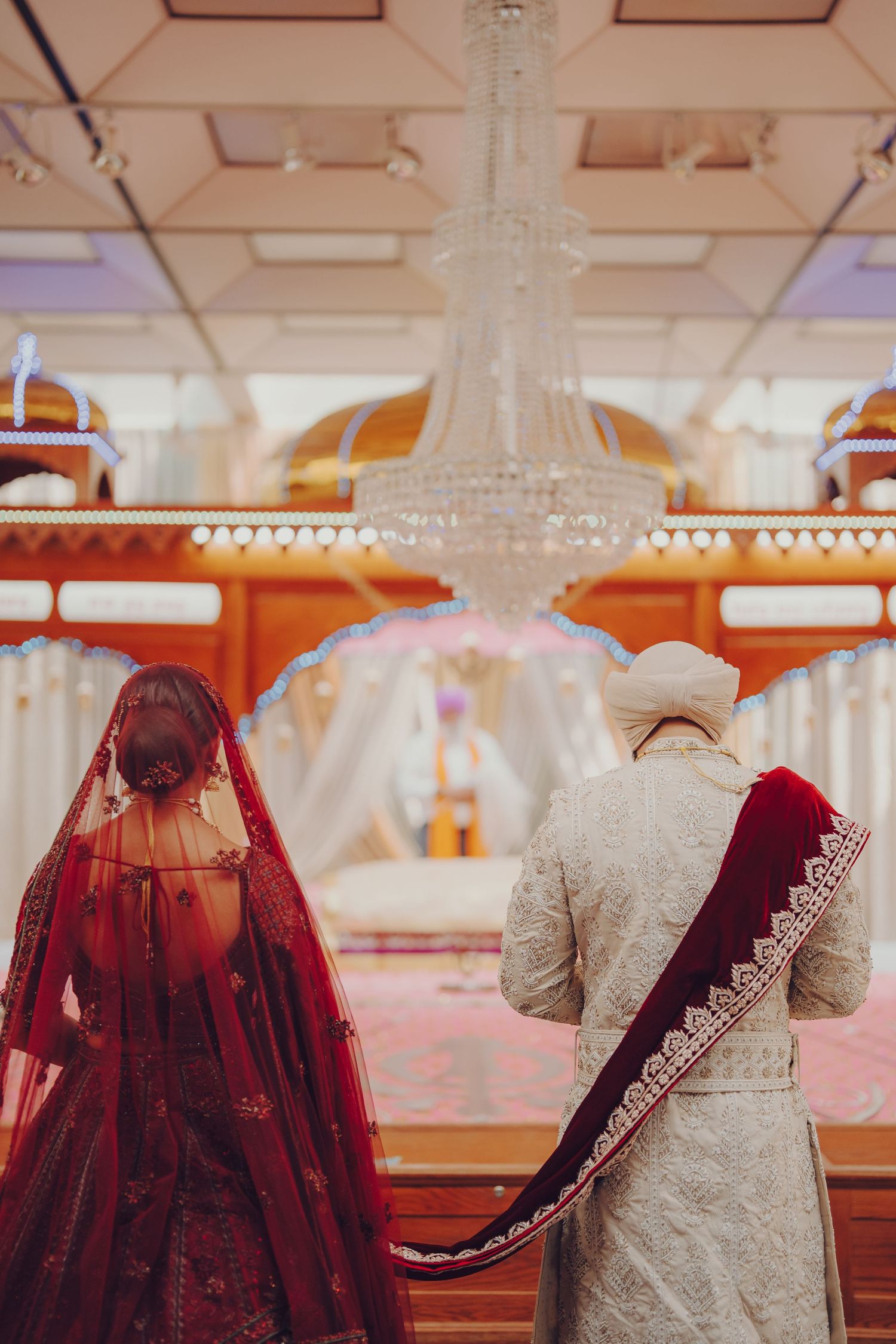 Side view of traditional wedding attire with burgundy lehenga and cream sherwani on display.