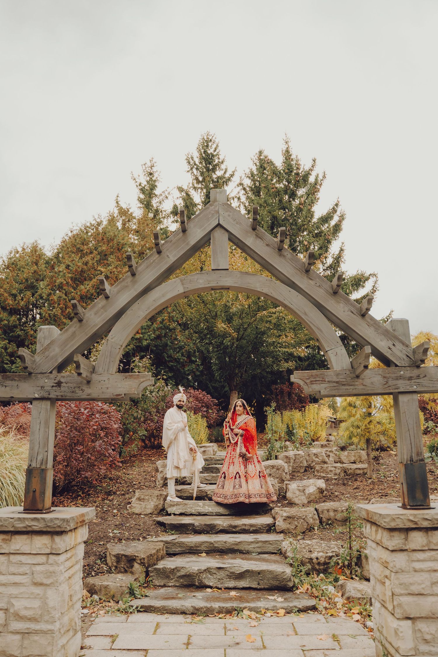 Stone archways line a garden pathway with autumn foliage and trees in the background.