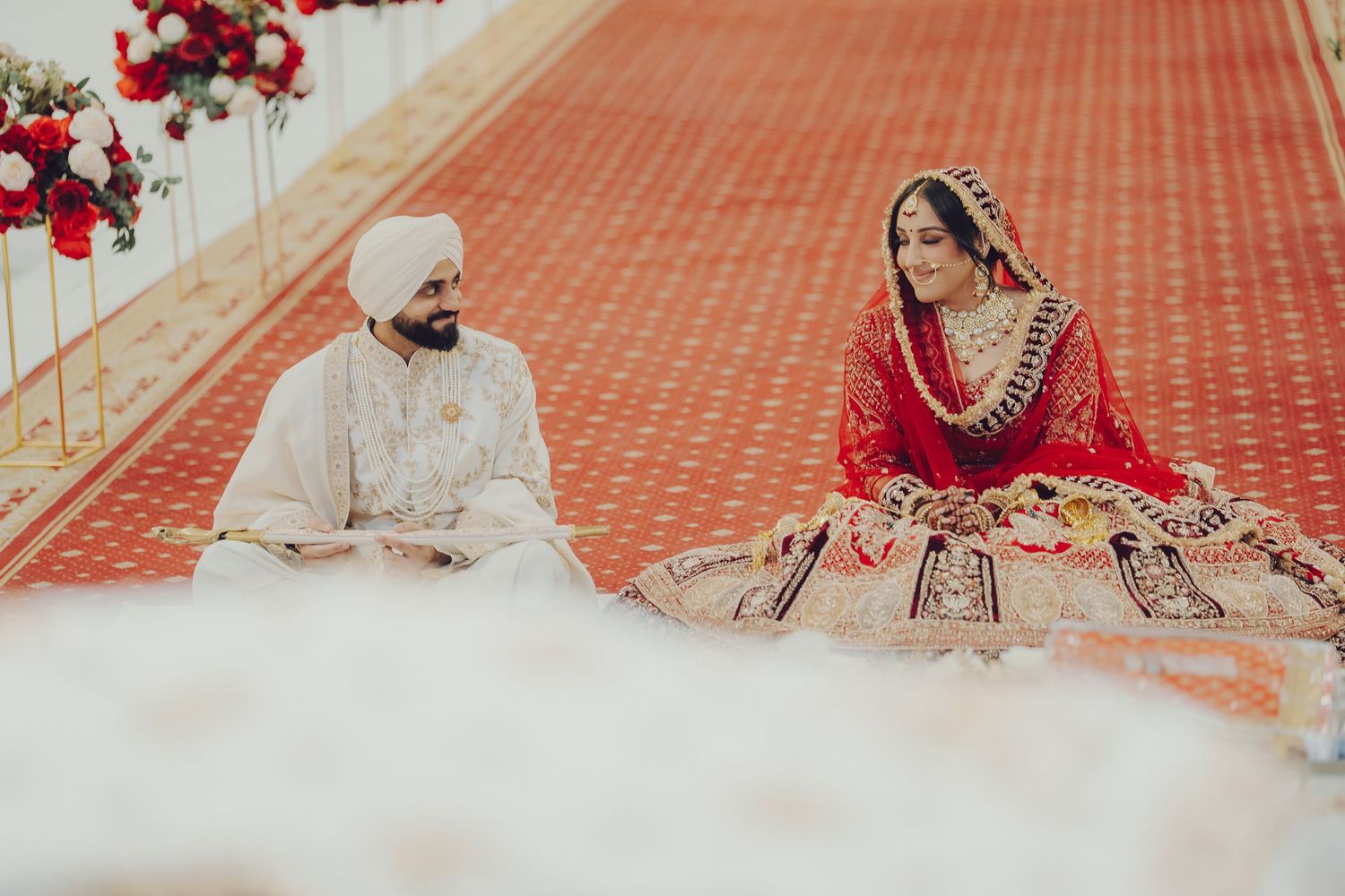Traditional Indian wedding couple seated on floor during ceremony in ornate red setting.