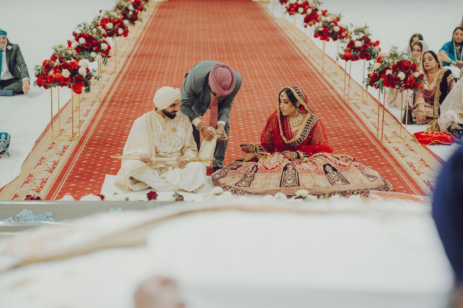 Traditional Sikh wedding ceremony setup with red floral decorations along the aisle.