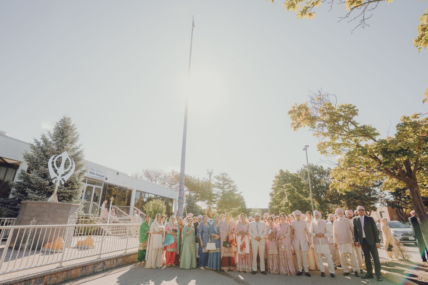 Large outdoor Sikh wedding ceremony gathering with guests in colorful attire under blue sky.