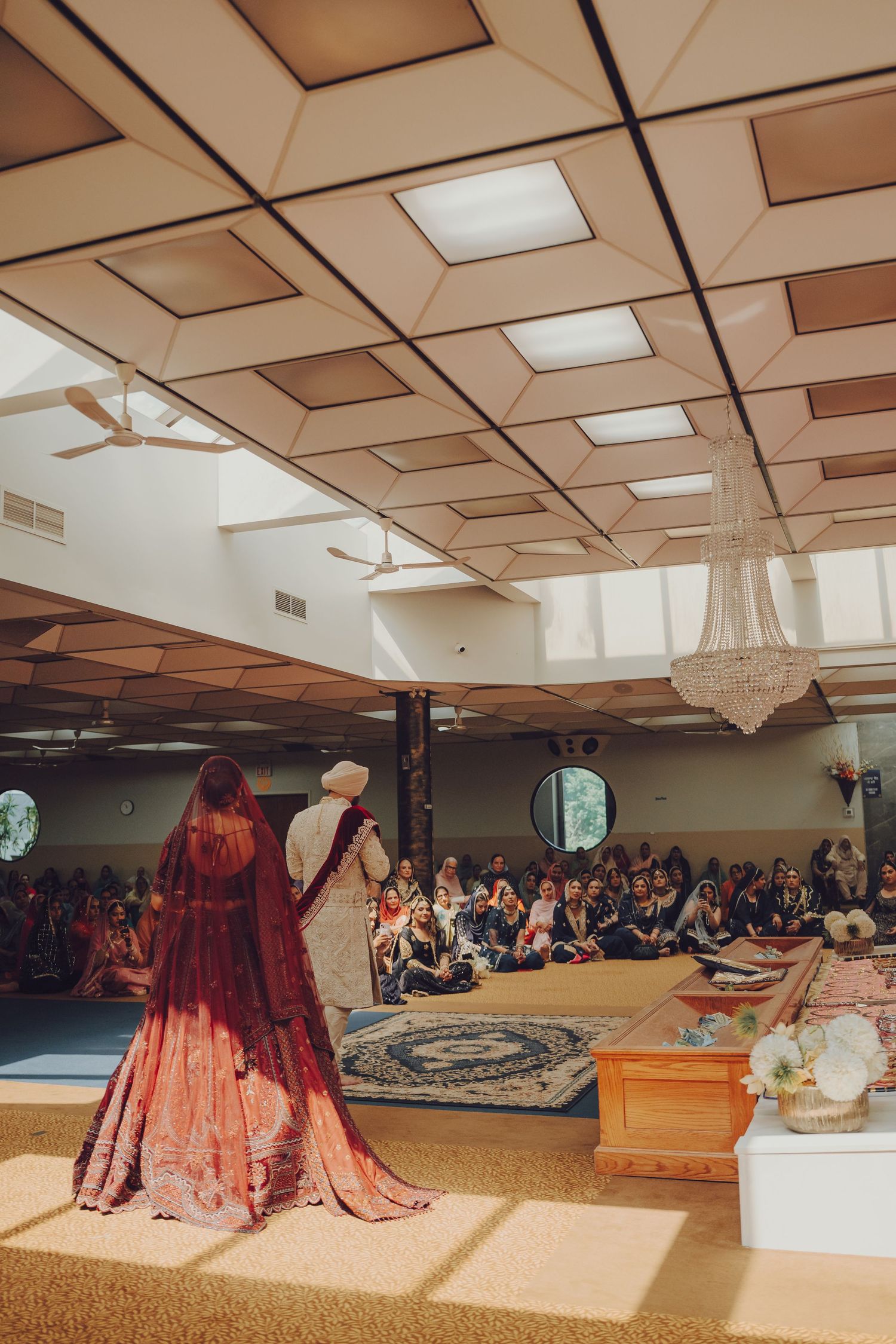 Wedding ceremony in a banquet hall with chandelier and gathered guests watching.