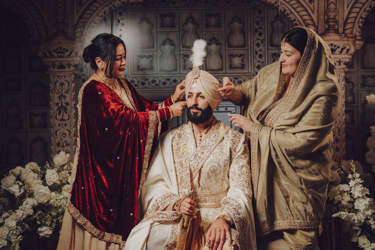 Indoor wedding ceremony with participants in traditional Sikh attire and floral decorations.