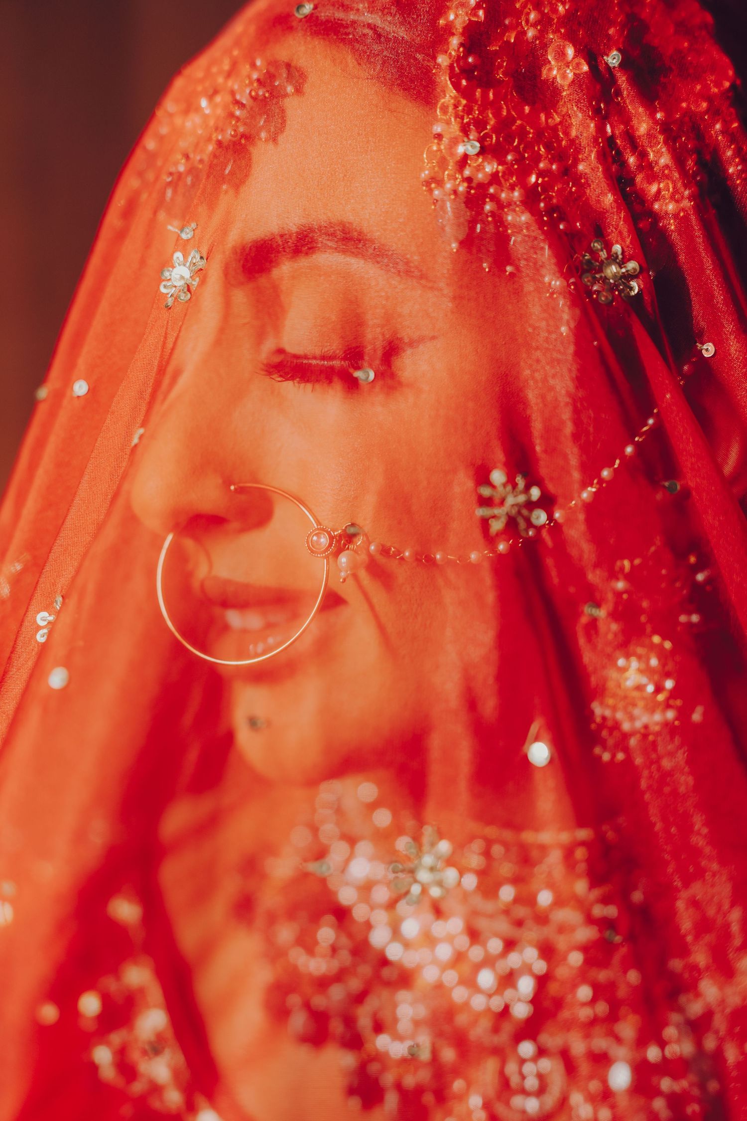 Close-up details of a traditional Indian bride's jewelry and veil in vibrant red with sparkling embellishments.