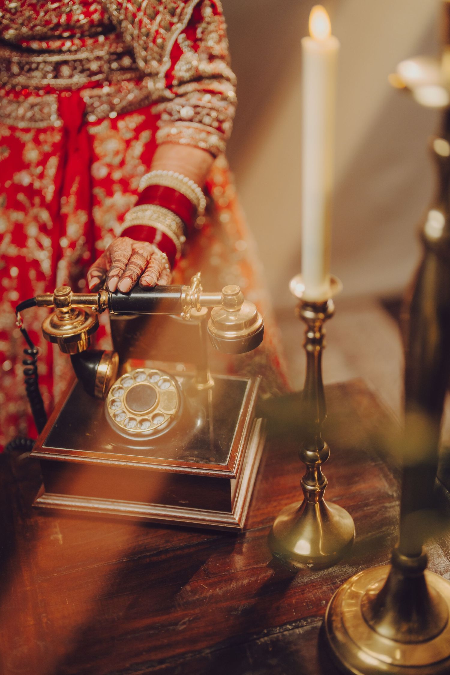 Vintage rotary telephone and candlestick on wooden table with traditional Indian bridal hands in frame.