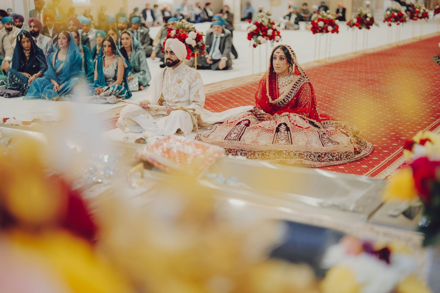 Colorful Indian wedding ceremony setup with guests seated on floor and decorative elements.