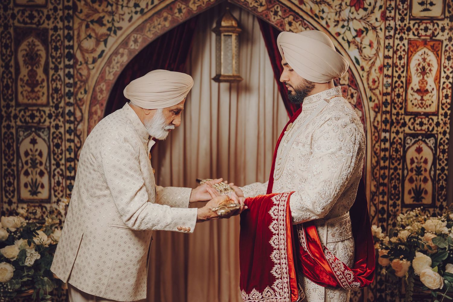 Traditional wedding ceremony with intricate cultural attire and decorative elements against ornate patterned backdrop.